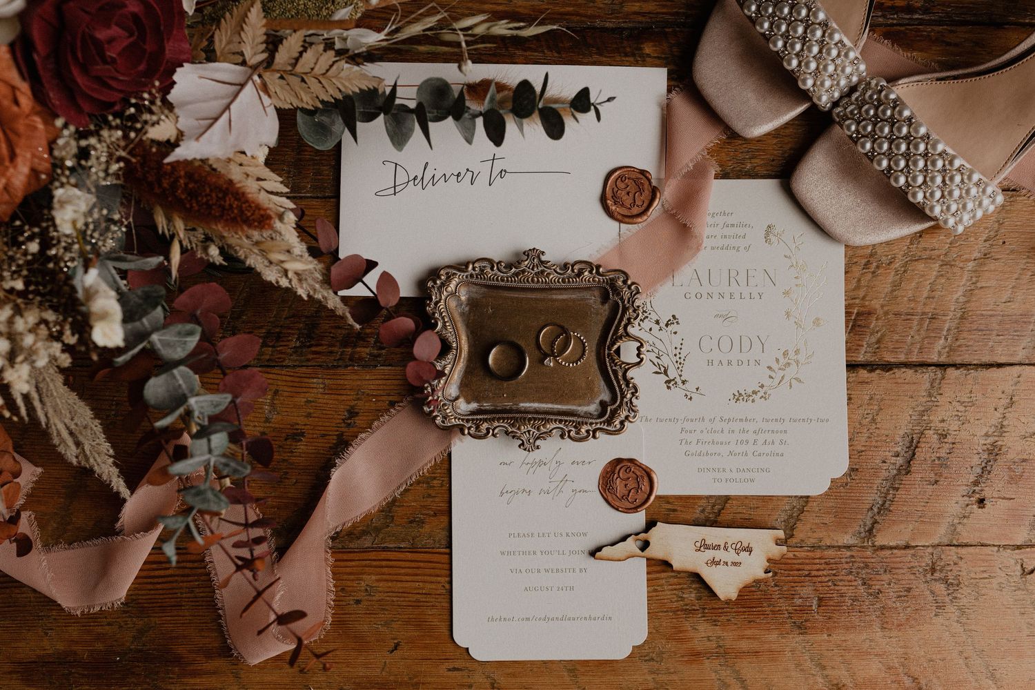 Wedding stationery and details arranged on a rustic wooden surface with floral elements.