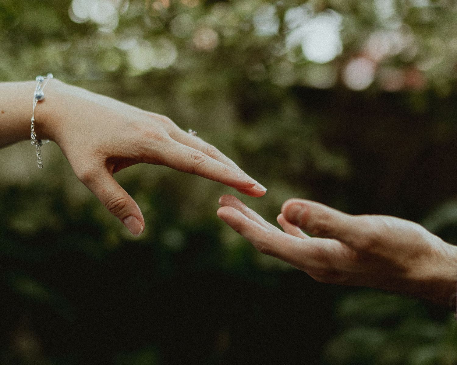 Close-up of hands reaching towards each other with soft natural bokeh background.