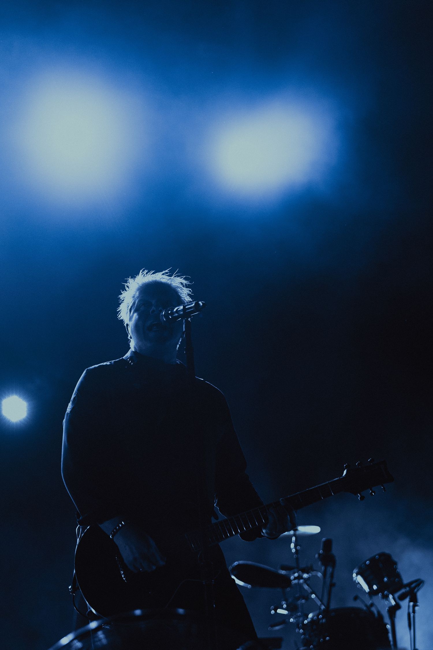 Silhouetted guitarist performs on stage against deep blue atmospheric lighting and fog.