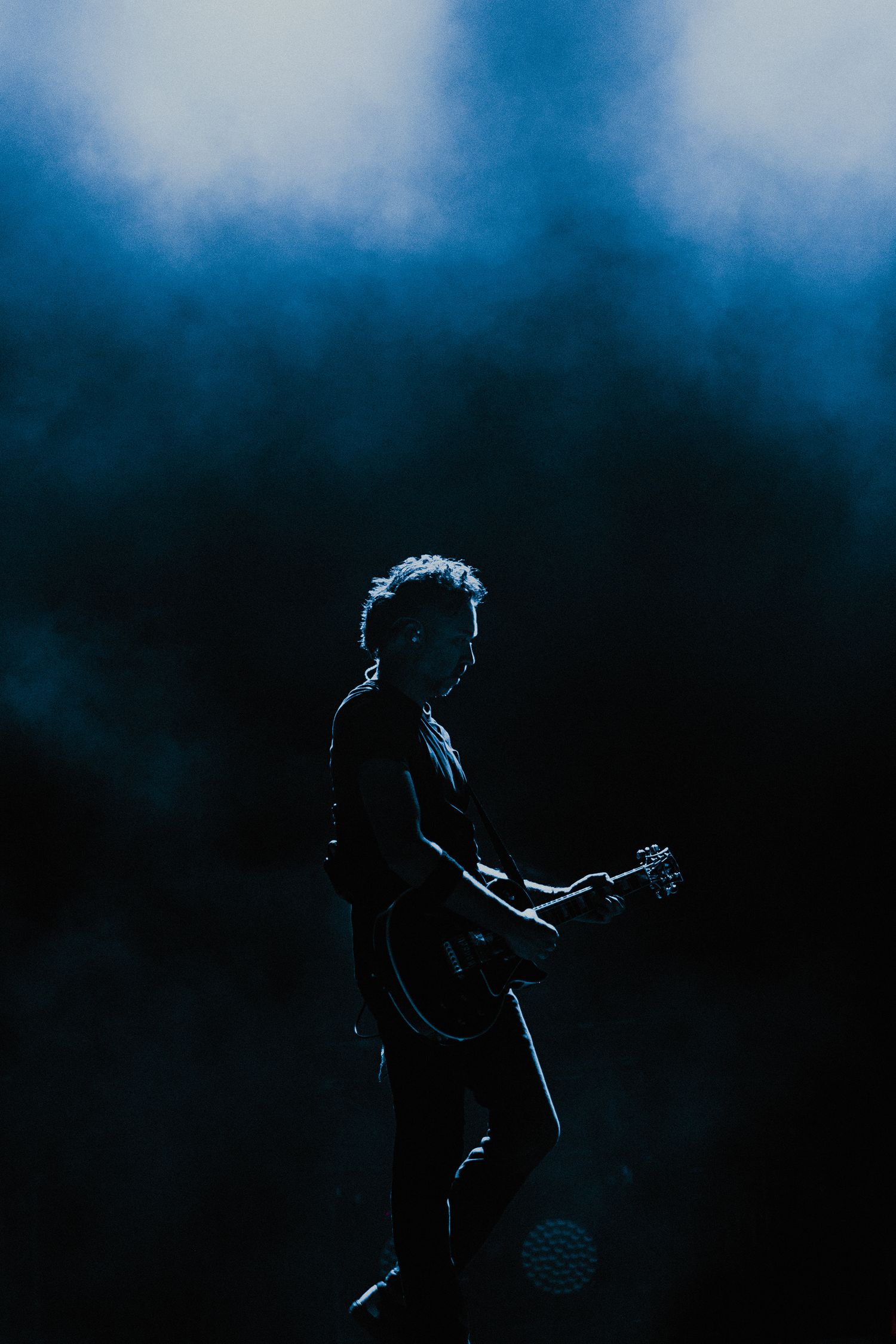 Silhouetted musician performs with guitar against moody blue stage lighting.