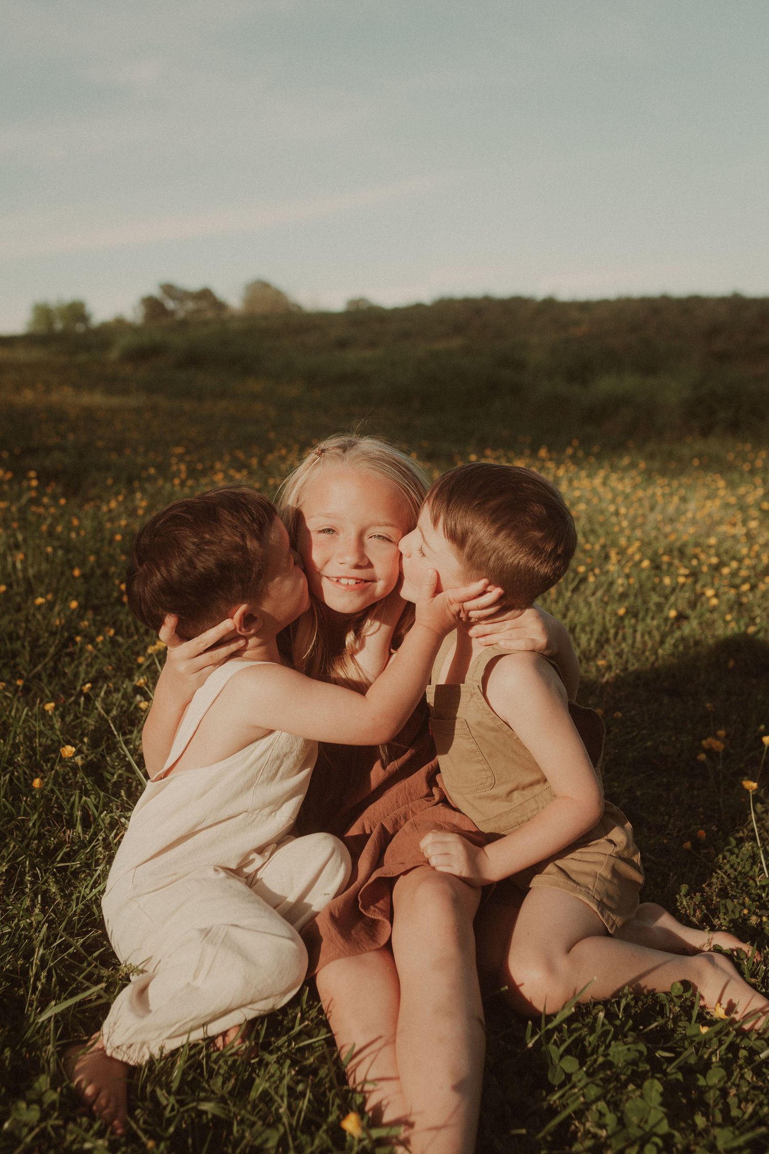 Children share sweet moments together in wildflower field at sunset.