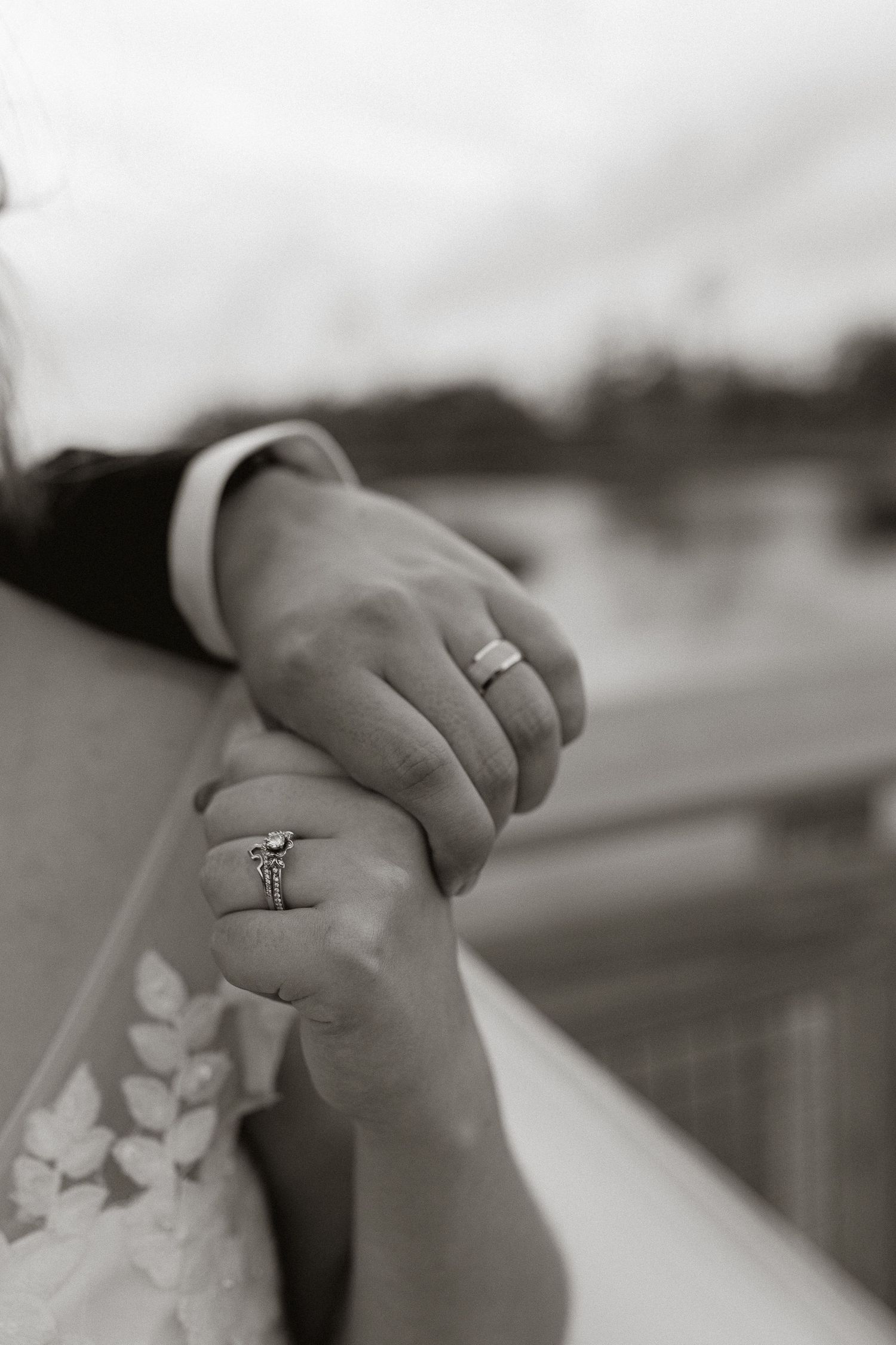 Close-up detail of hands with wedding rings and delicate lace fabric.