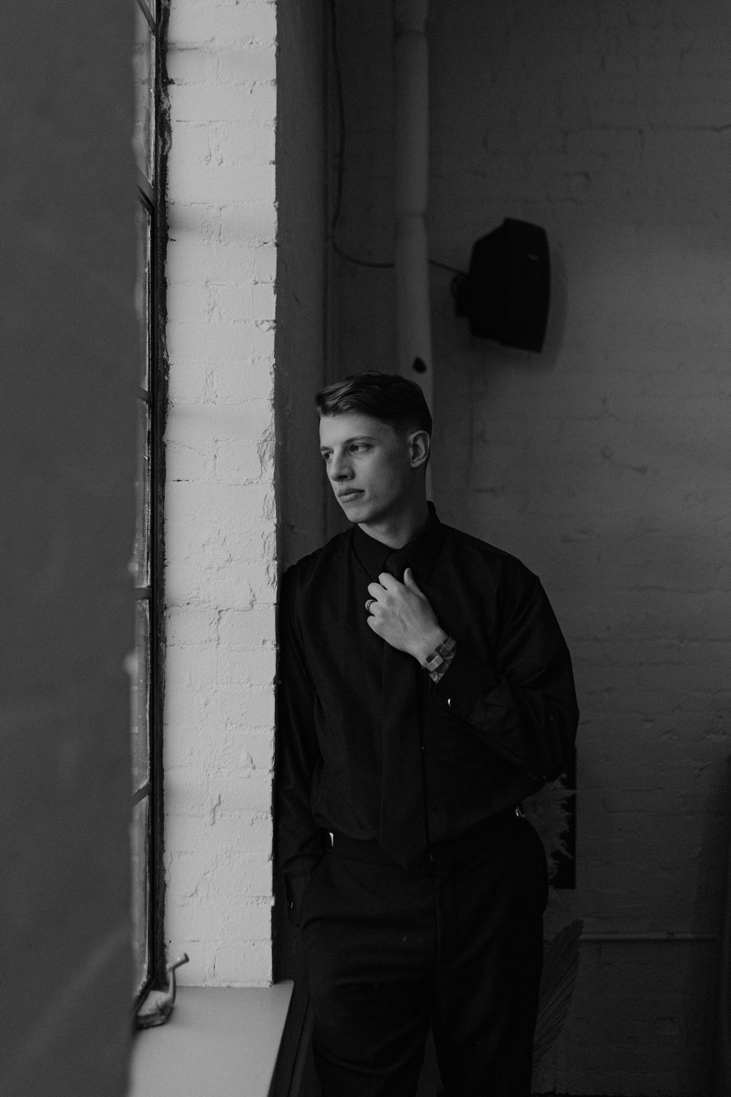 Dramatic black and white portrait against a white brick wall in moody lighting.