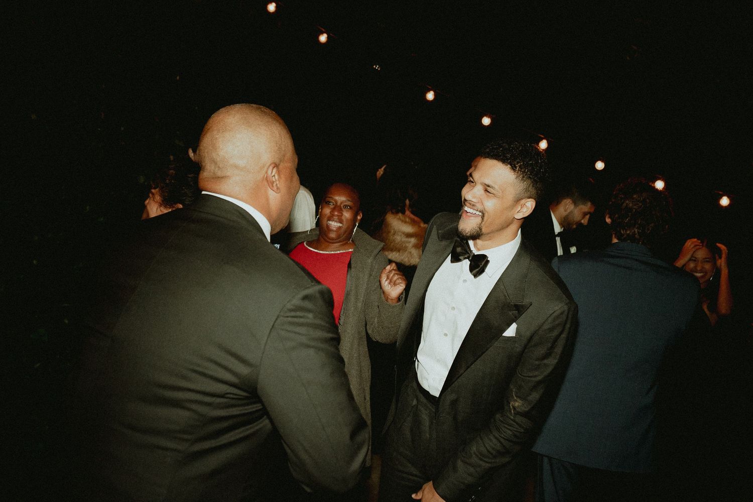 A group of people in formal attire interact at a dimly lit social gathering or event.