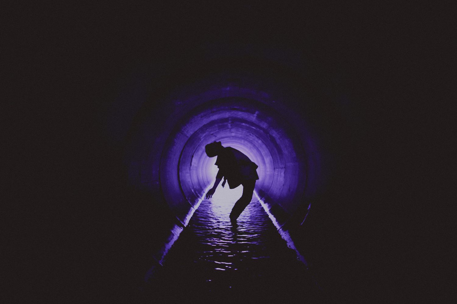 Silhouette of a person crouching in a dark tunnel with purple neon lighting.