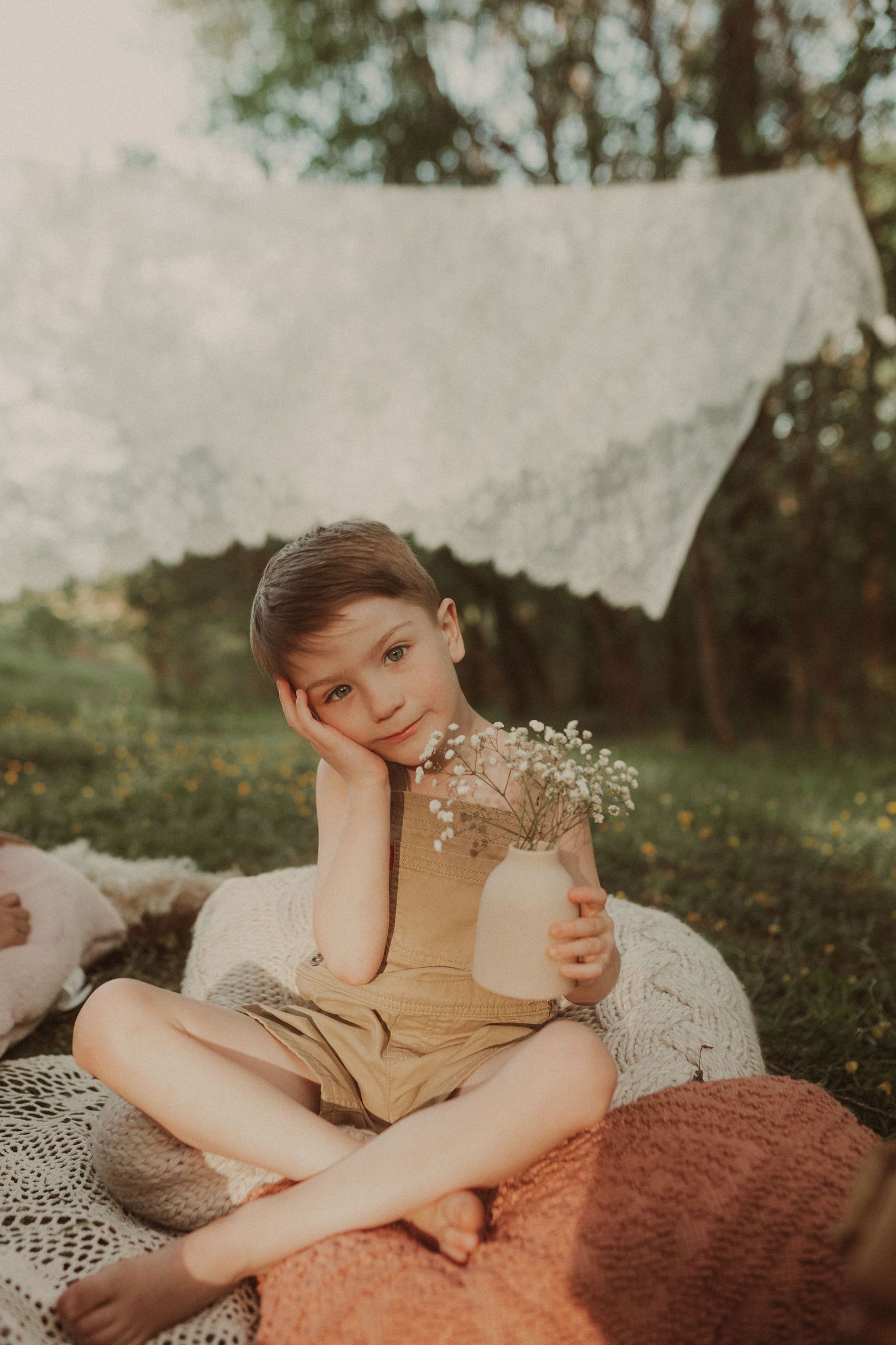 Person rests on blanket holding delicate flowers in outdoor setting.