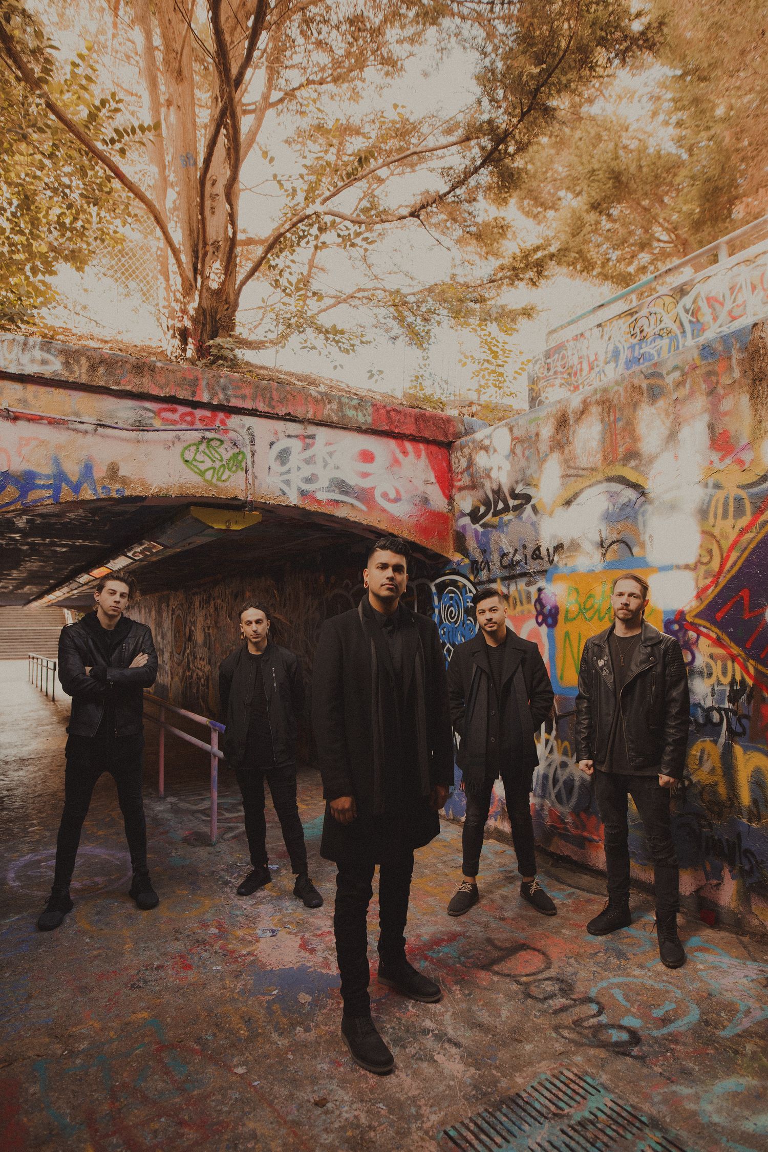 Band members arranged in a panoramic shot against graffiti-covered walls in an urban setting.