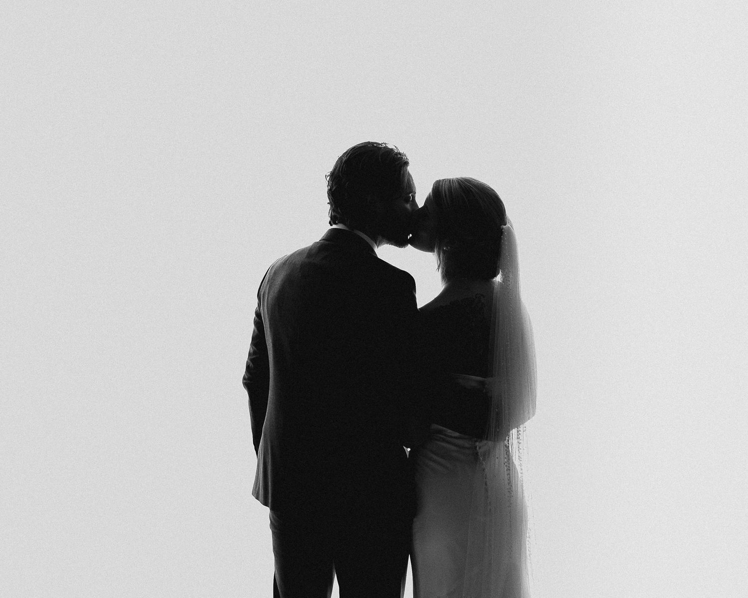 Black and white silhouette of a couple sharing a romantic kiss, captured in a minimalist wedding portrait.