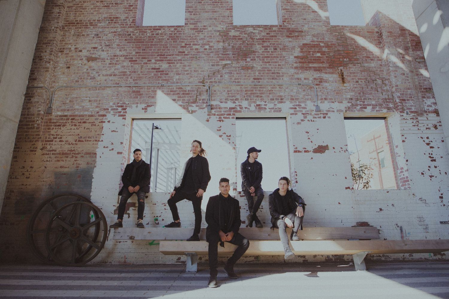 A group poses against a weathered brick wall in an industrial setting.