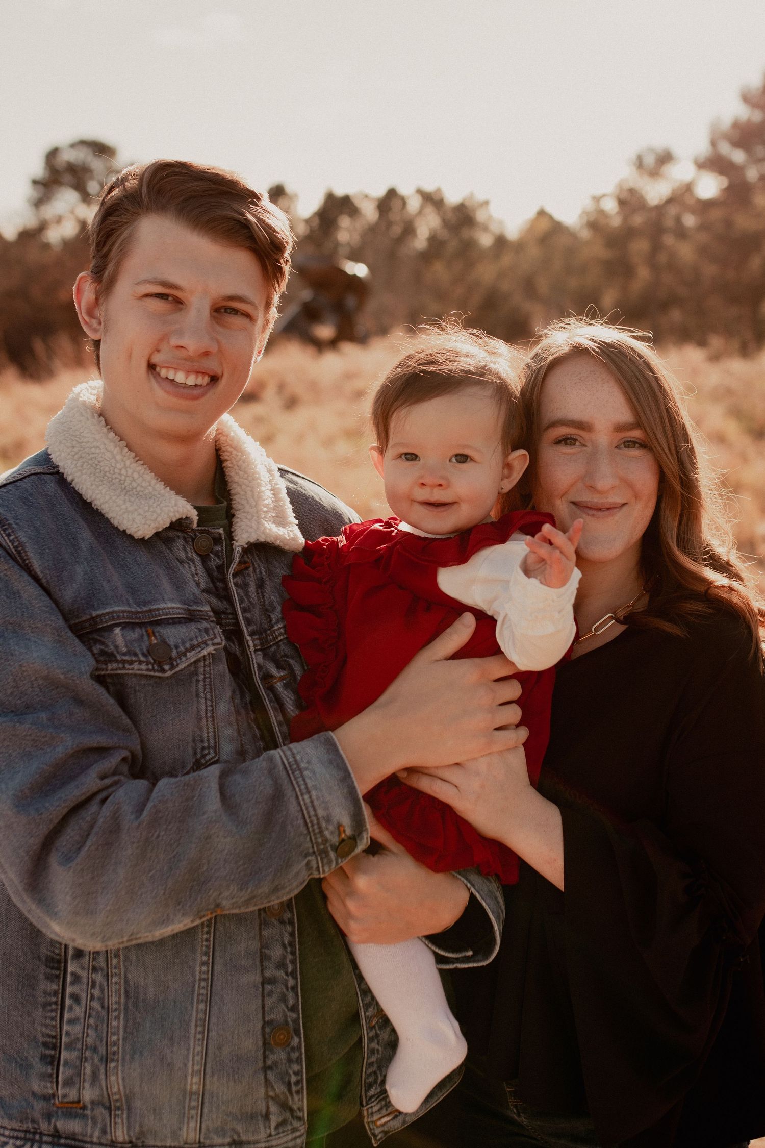 Winter family photoshoot with denim and red outfits against a warm sunset backdrop.
