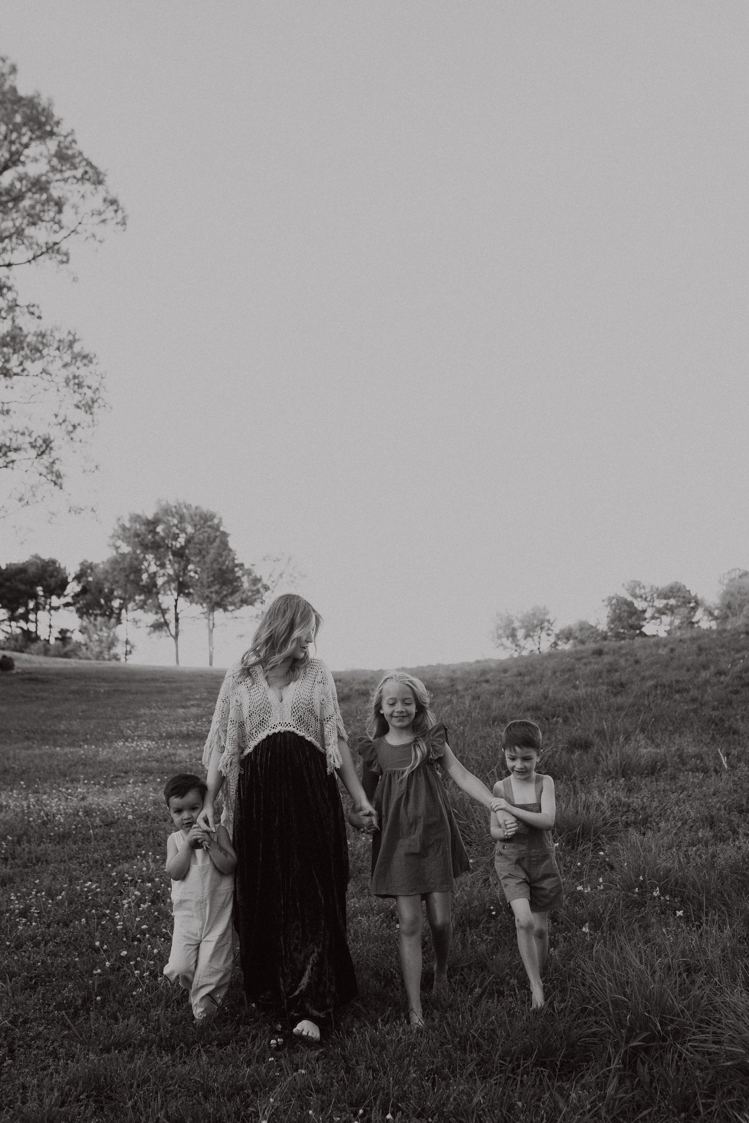 Children play together on grassy hillside in black and white photograph.
