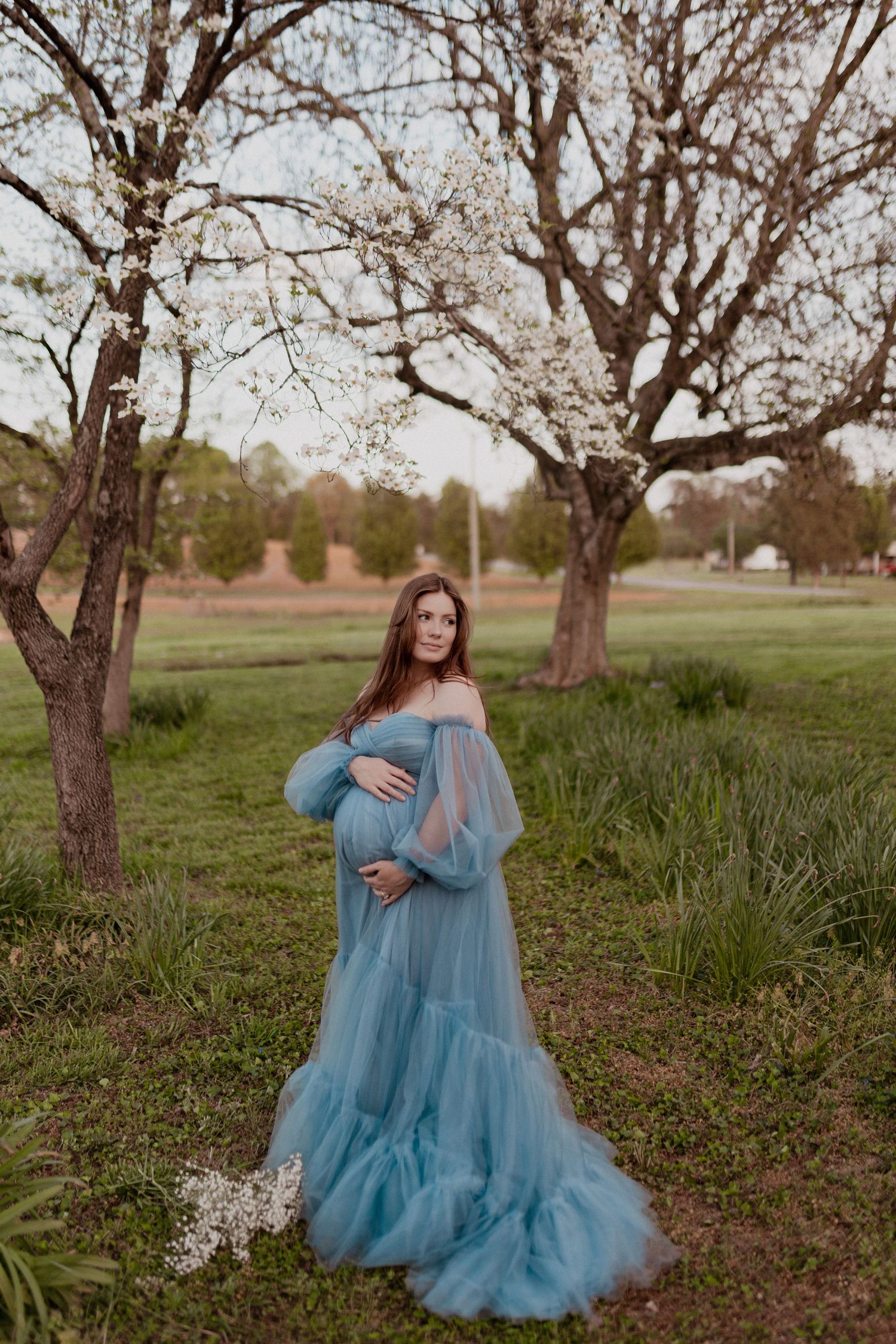 Two people in ethereal blue dresses share a tender moment among blooming spring trees.