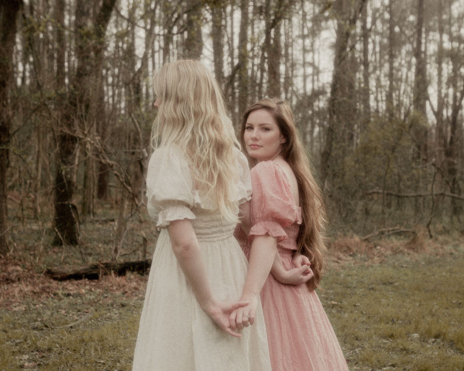 Dreamy portrait of two people in vintage dresses walking through misty forest.