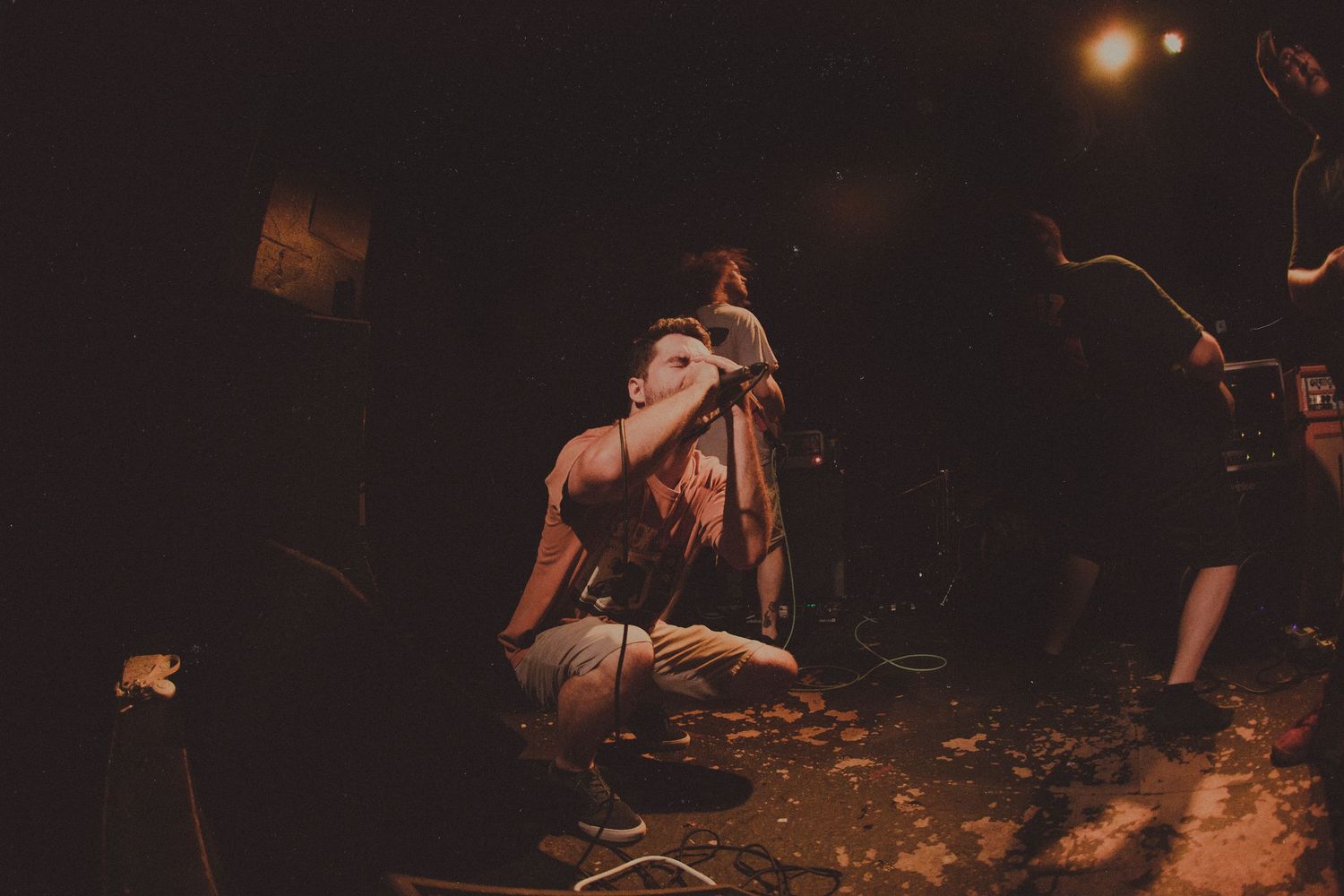 Dark atmospheric concert venue with crowd and performers in dim lighting.