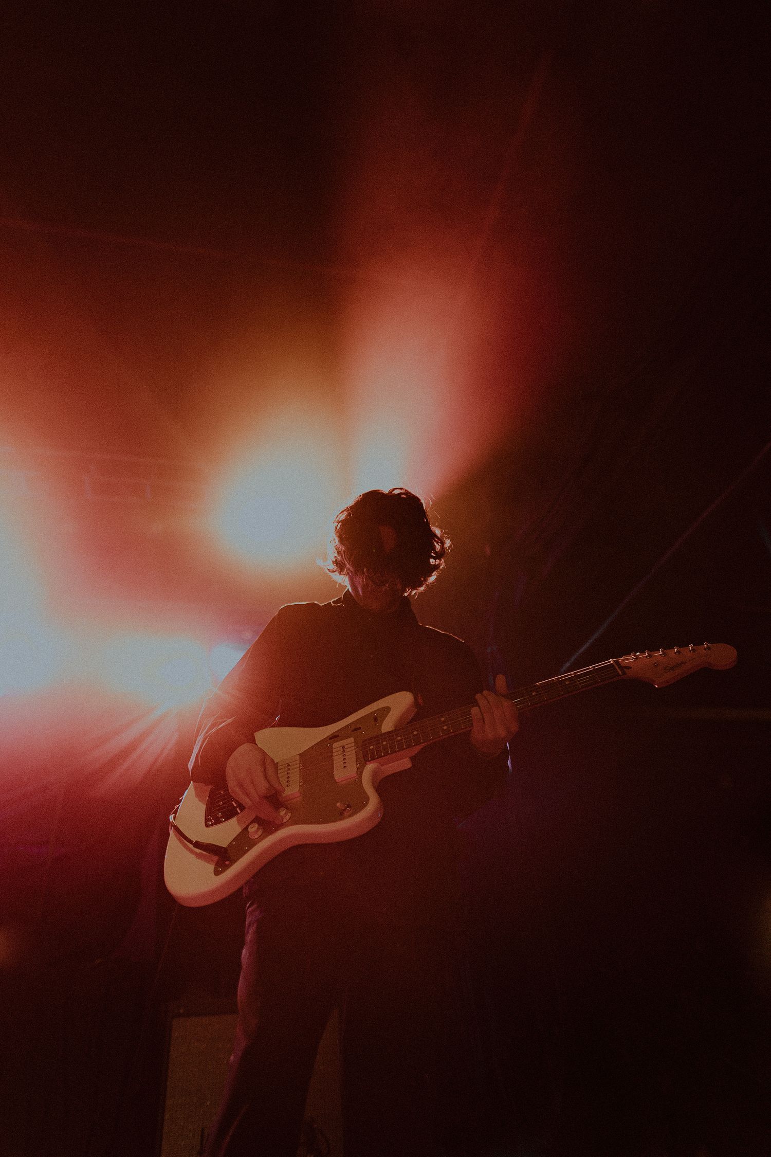 Silhouetted guitarist playing under warm red stage lighting effects.