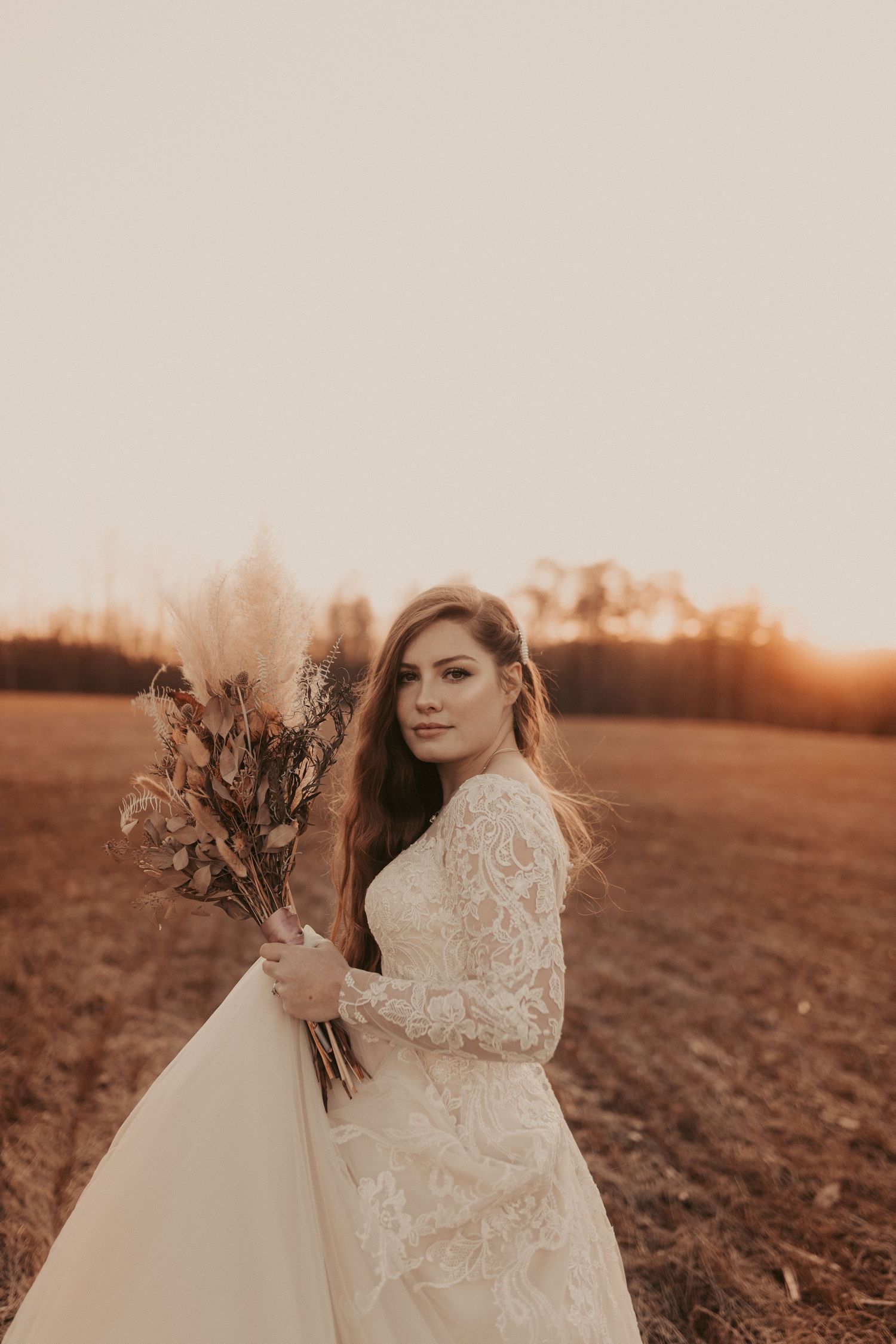 A bride in a lace gown poses with her bouquet during golden hour.