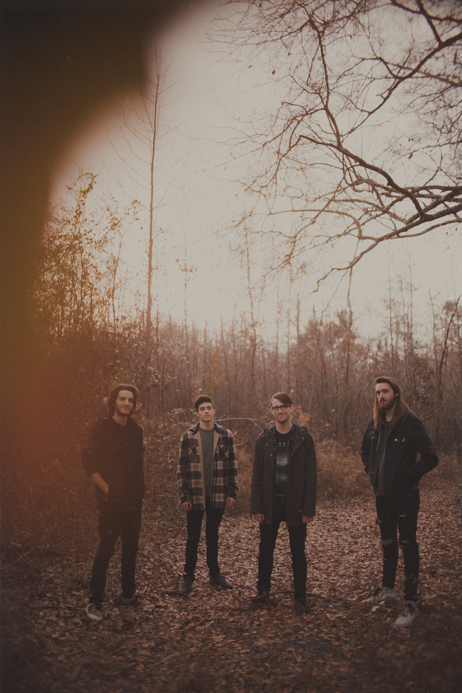 Band members standing in a line outdoors during autumn with bare trees in sepia tones.