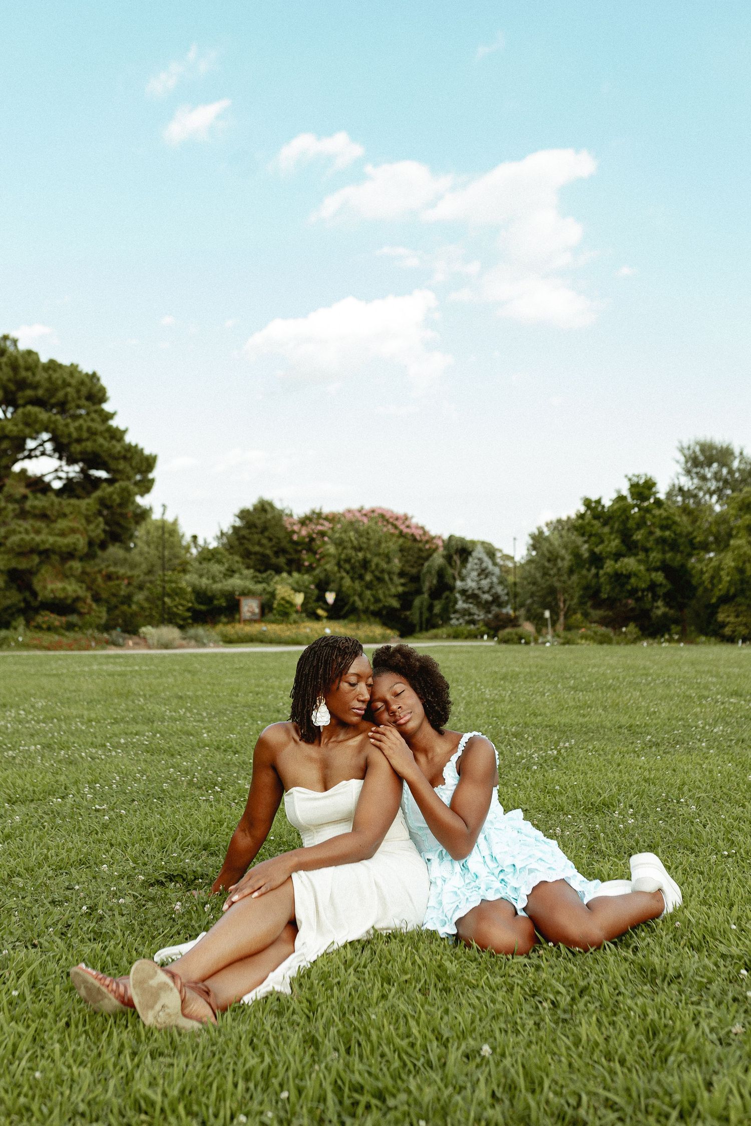 Two people in summer dresses sharing an intimate moment on green grass.