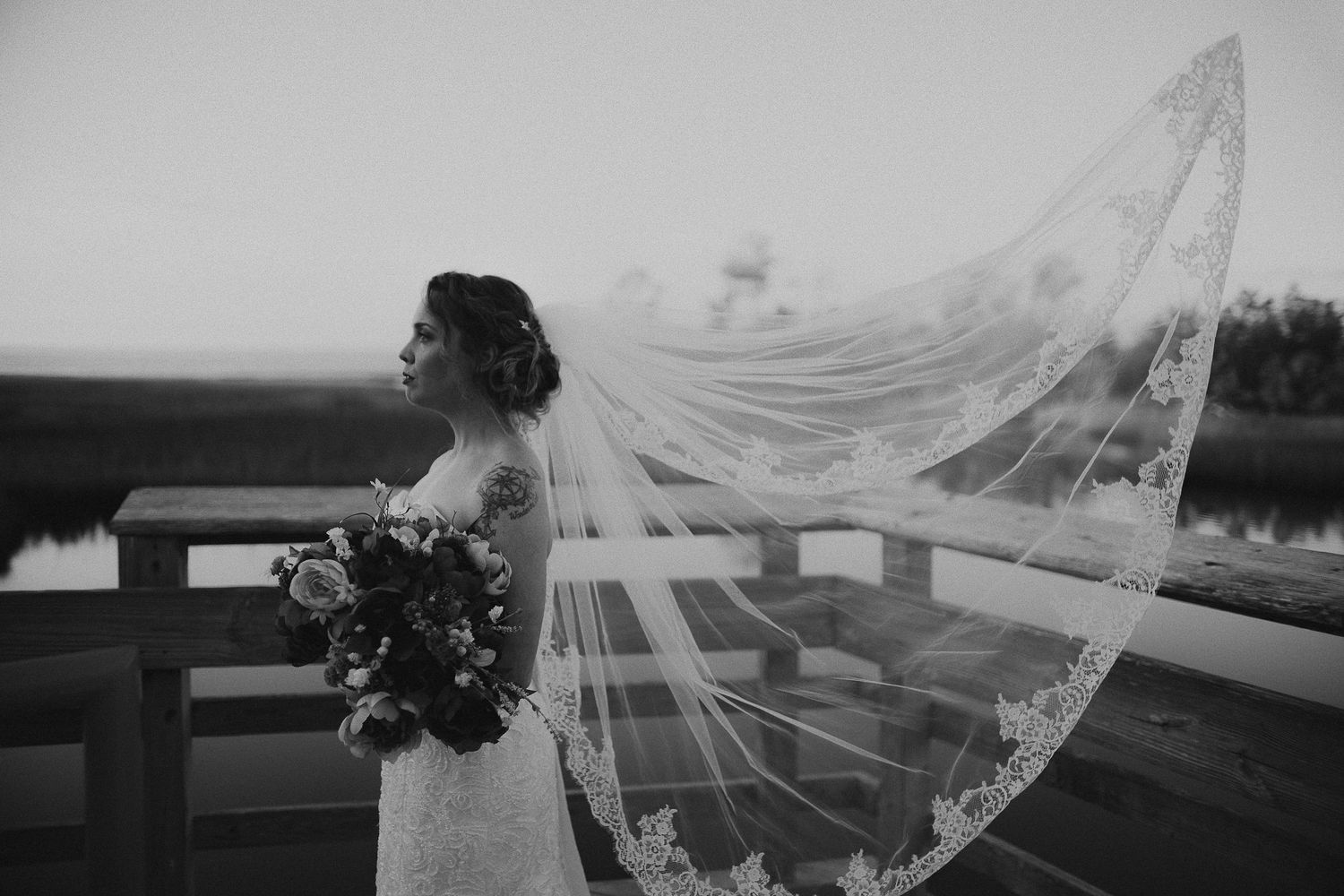 A flowing wedding veil catches the wind against a dramatic outdoor backdrop.