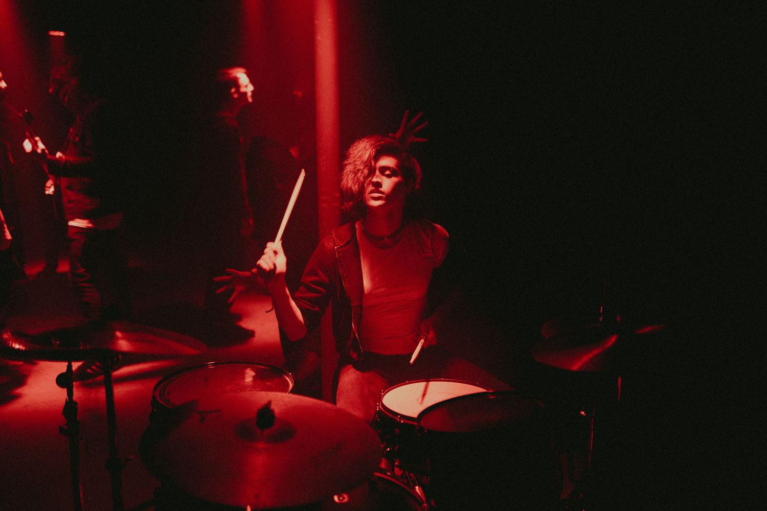 Deep red stage lighting creates dramatic atmosphere during a live musical performance.