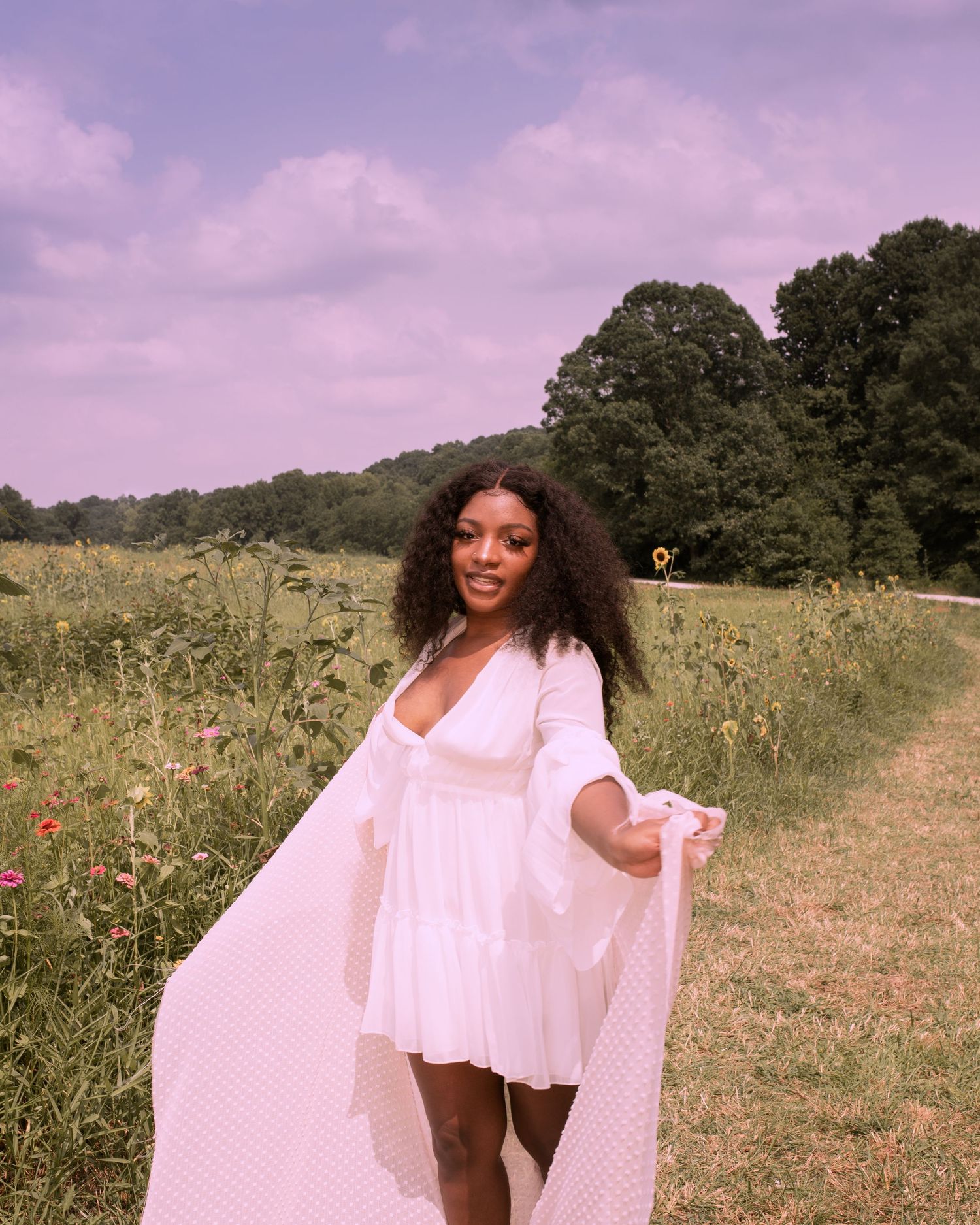 A person in a flowing white dress poses joyfully in a summer wildflower field.