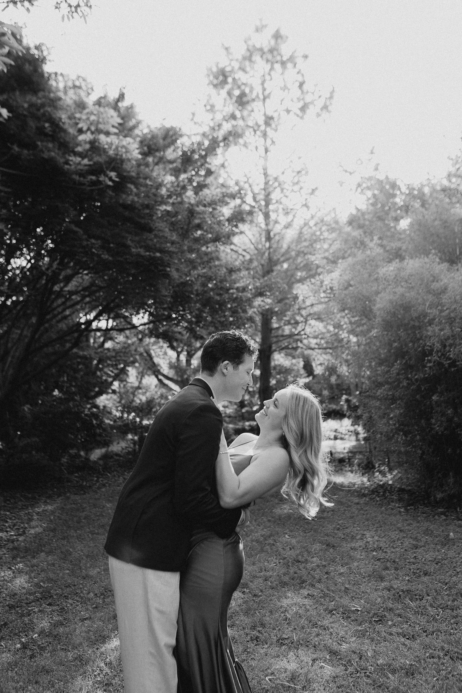 Black and white photo of a couple sharing a romantic moment in a lush garden setting.