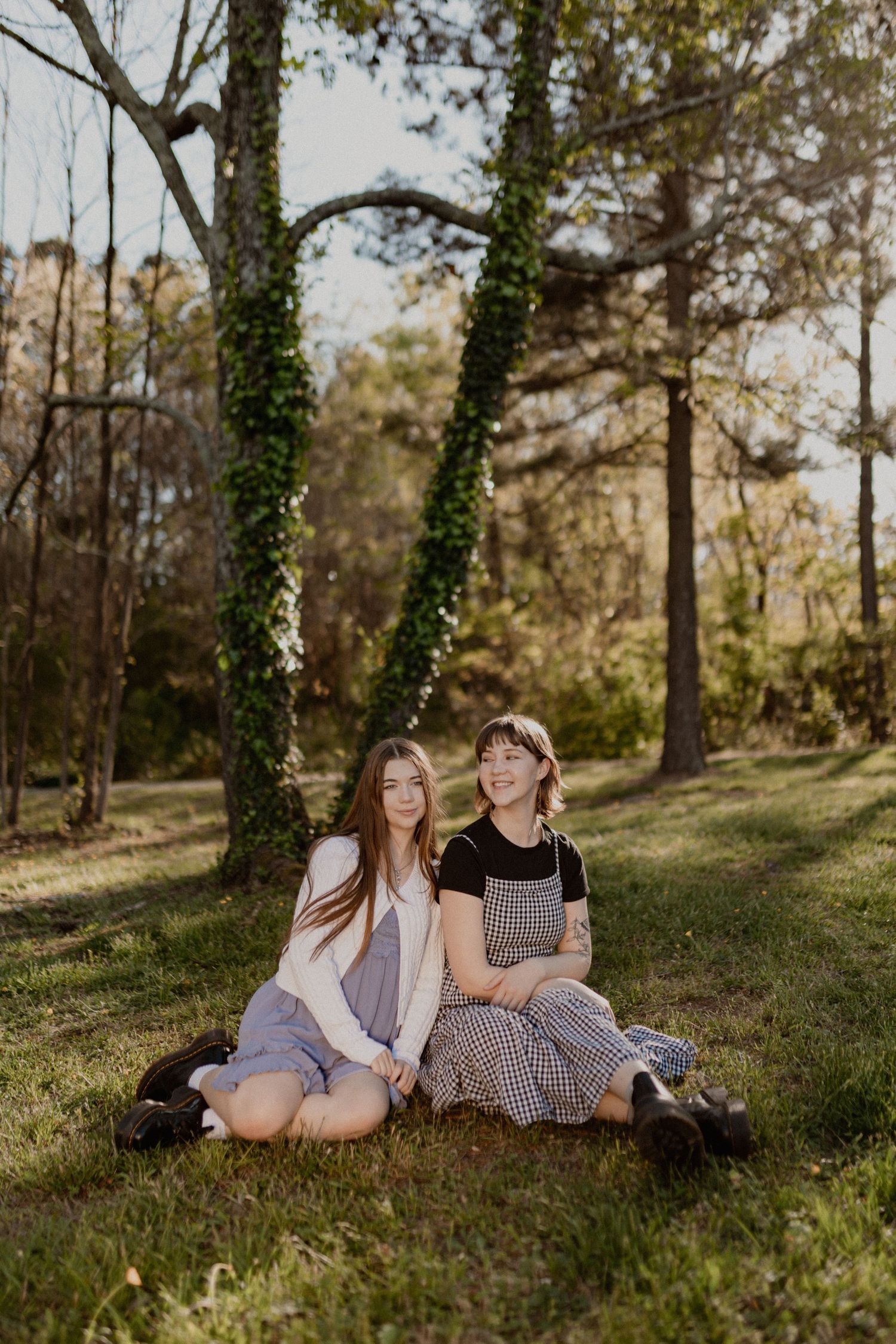 Friends relaxing together on grassy hillside in casual dresses.