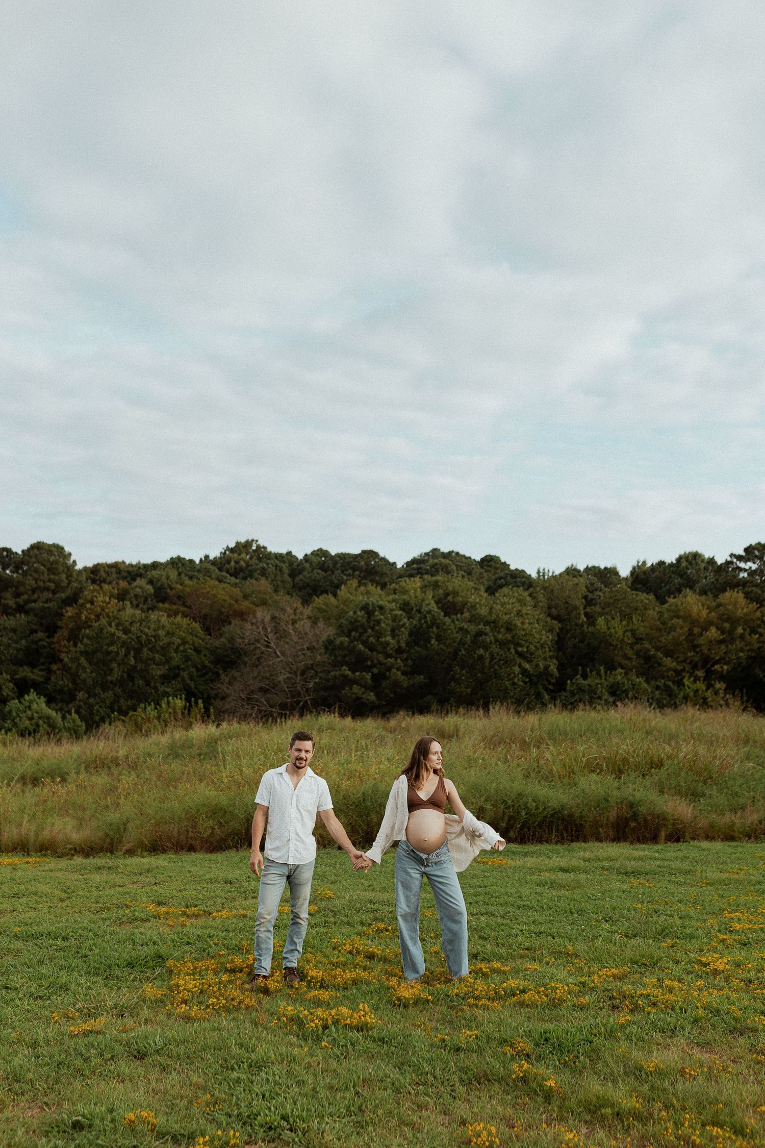 Couple standing together in a meadow with wildflowers under cloudy skies.