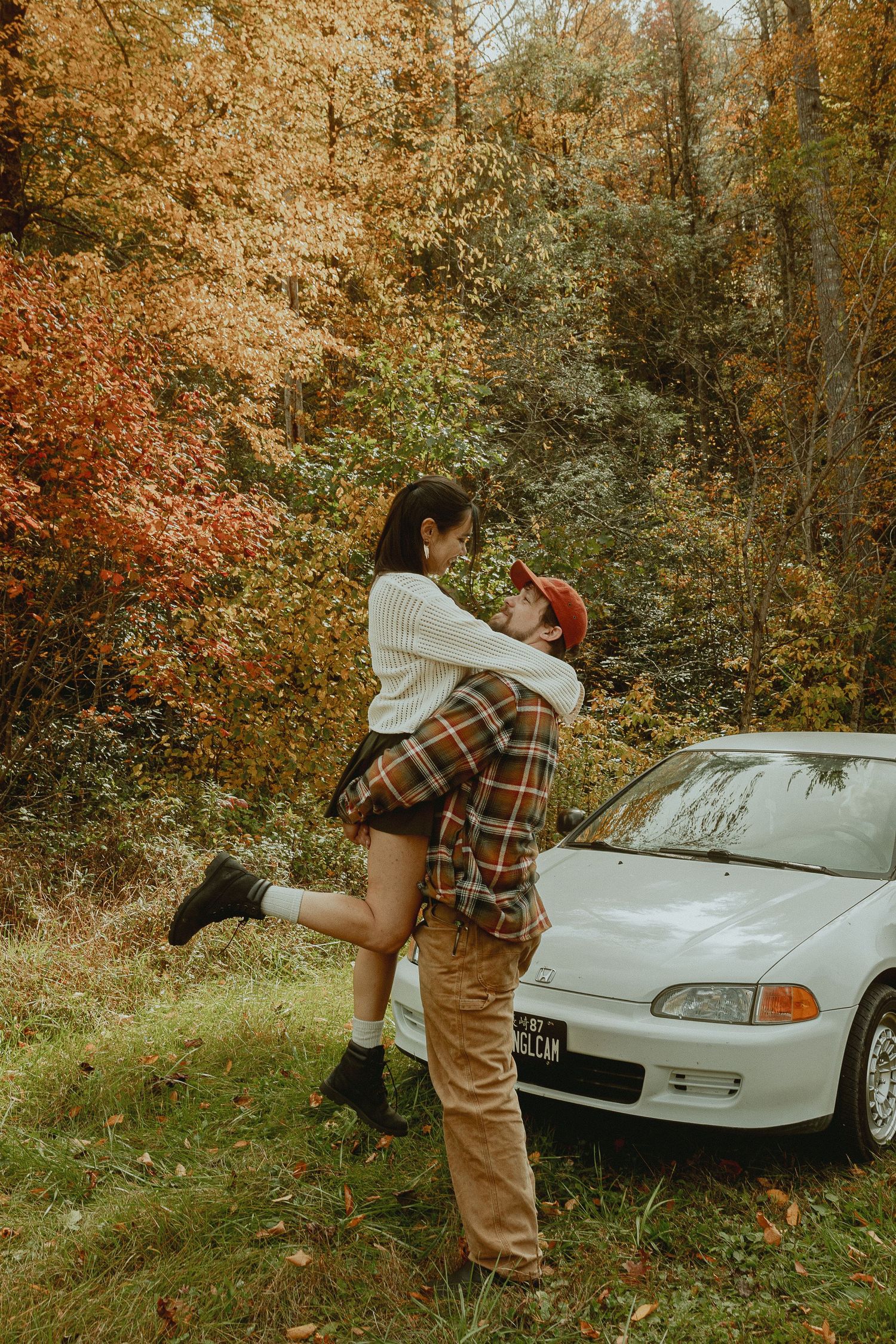 Playful engagement photo sequence with couple and white car against autumn trees.