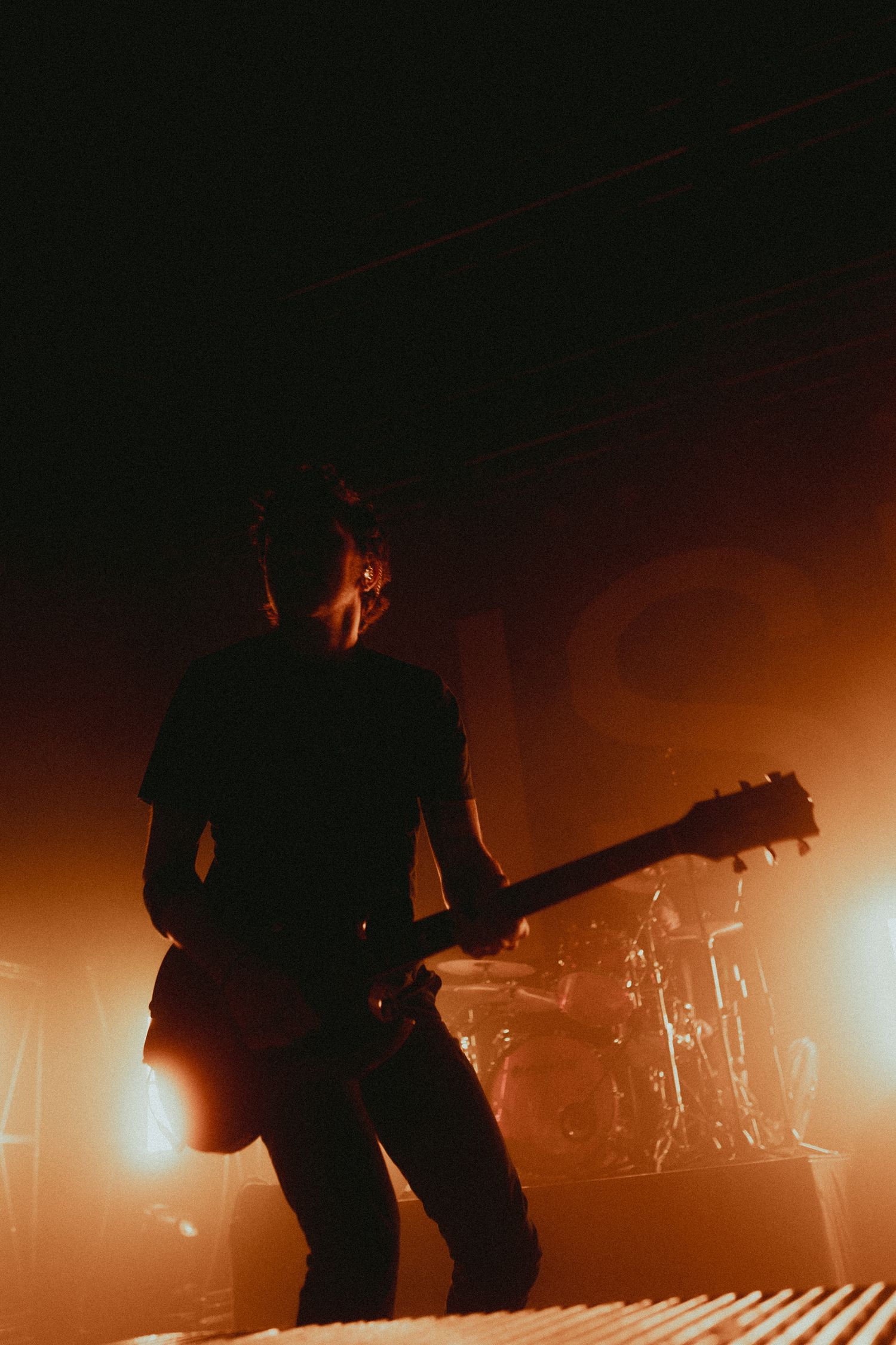 Silhouetted band members performing on stage with warm orange backlighting creating dramatic atmosphere.