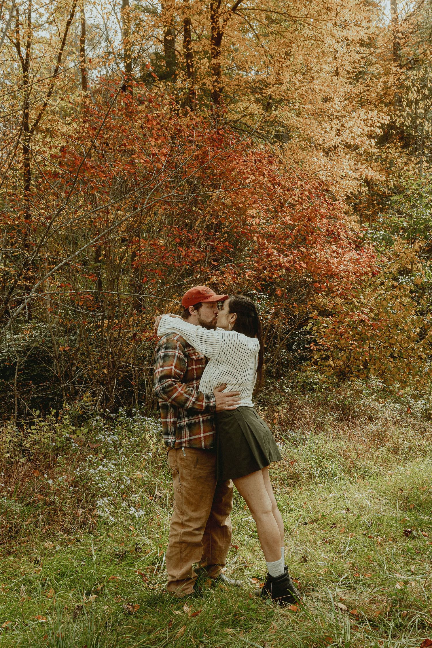 Romantic autumn engagement photos with couple in casual attire among fall foliage.