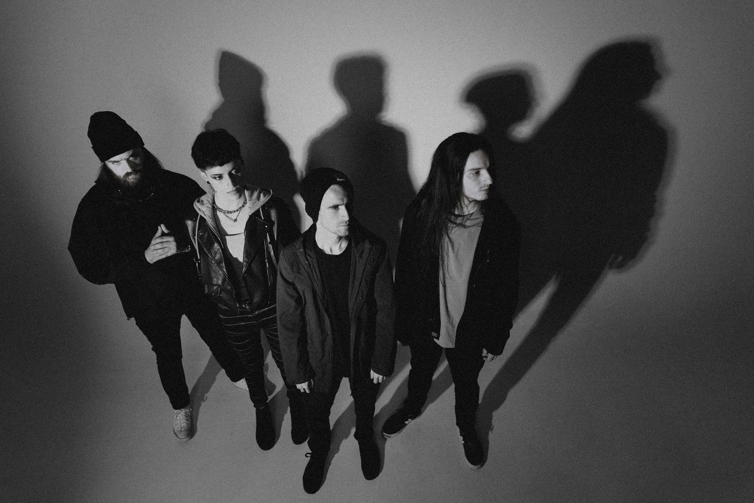 Black and white portrait of a rock band with dramatic shadows against a light background.