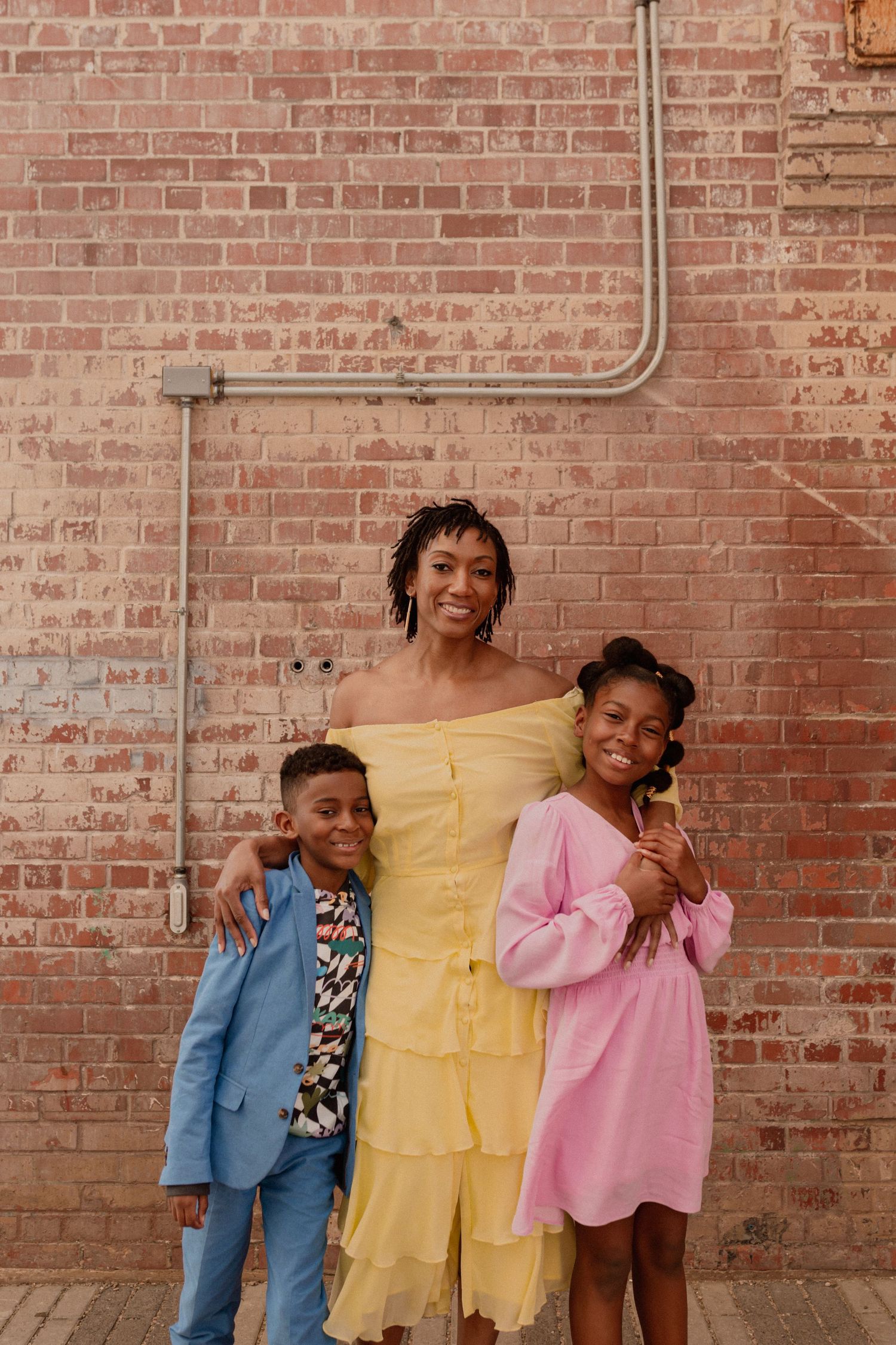 People in vibrant blue and pink outfits posing playfully against rustic brick wall.