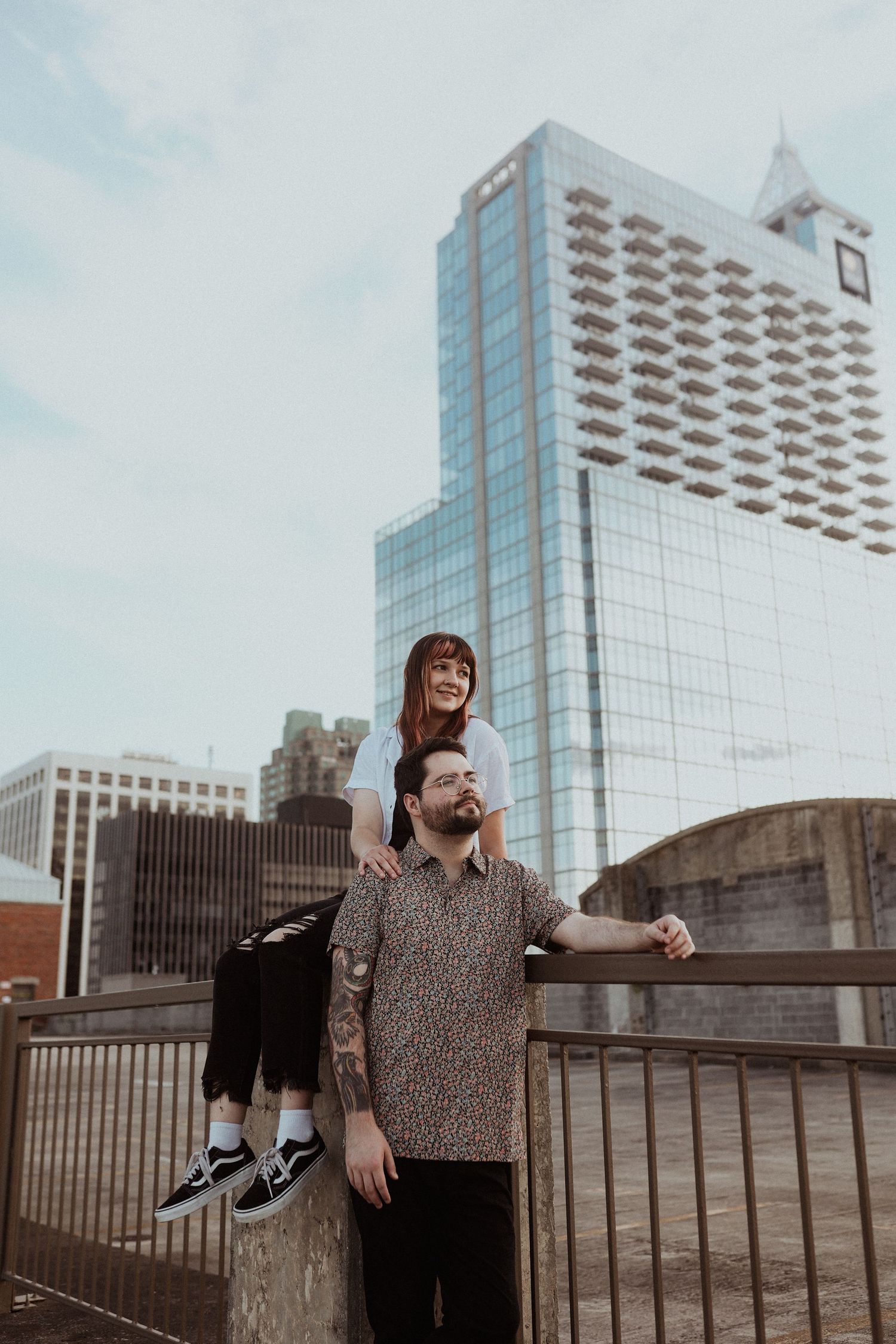 A couple poses playfully on an urban rooftop with modern buildings in the background.