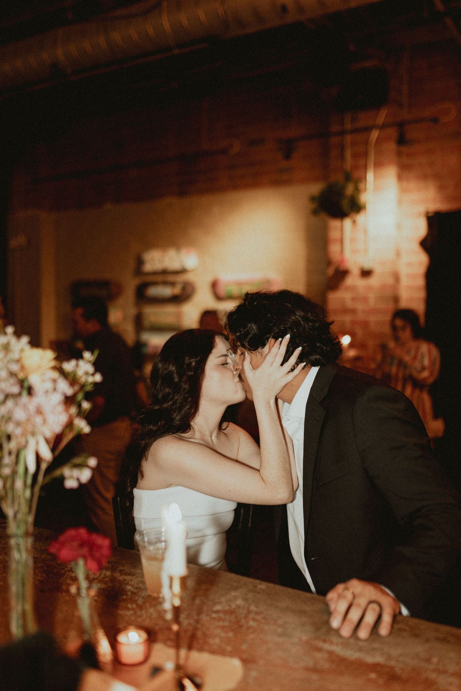 A romantic candlelit scene shows a couple sharing a kiss at a rustic reception venue.