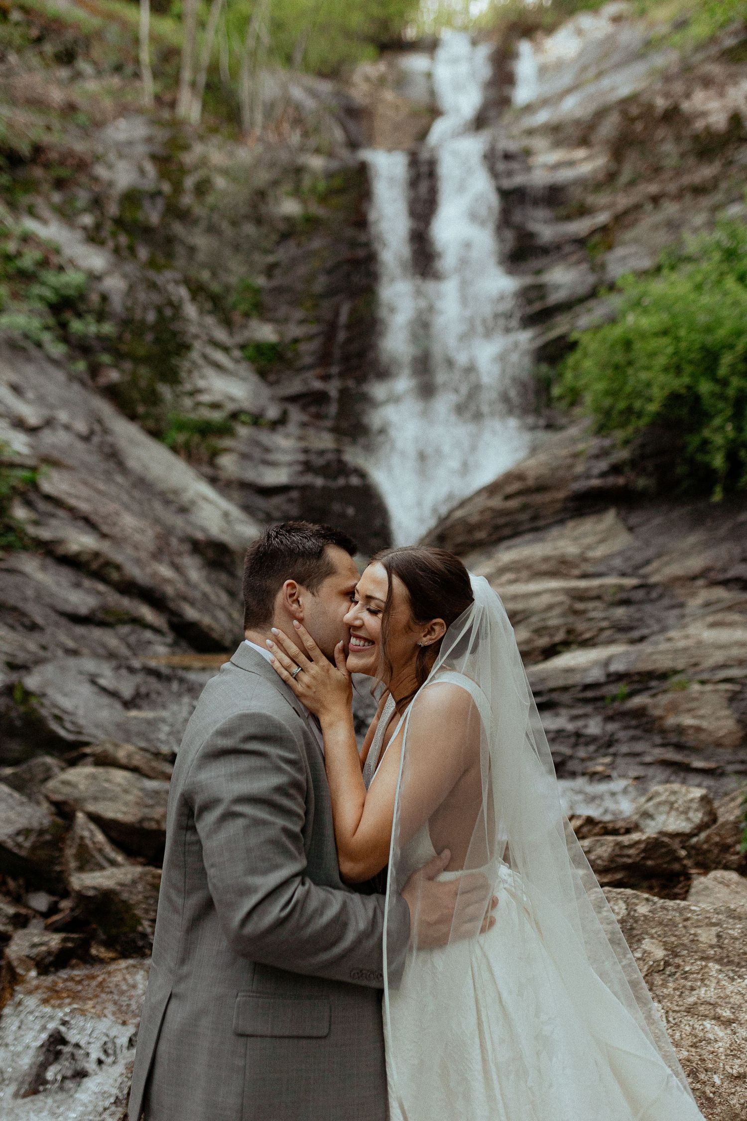 A tender moment between newlyweds captured against a dramatic waterfall backdrop.
