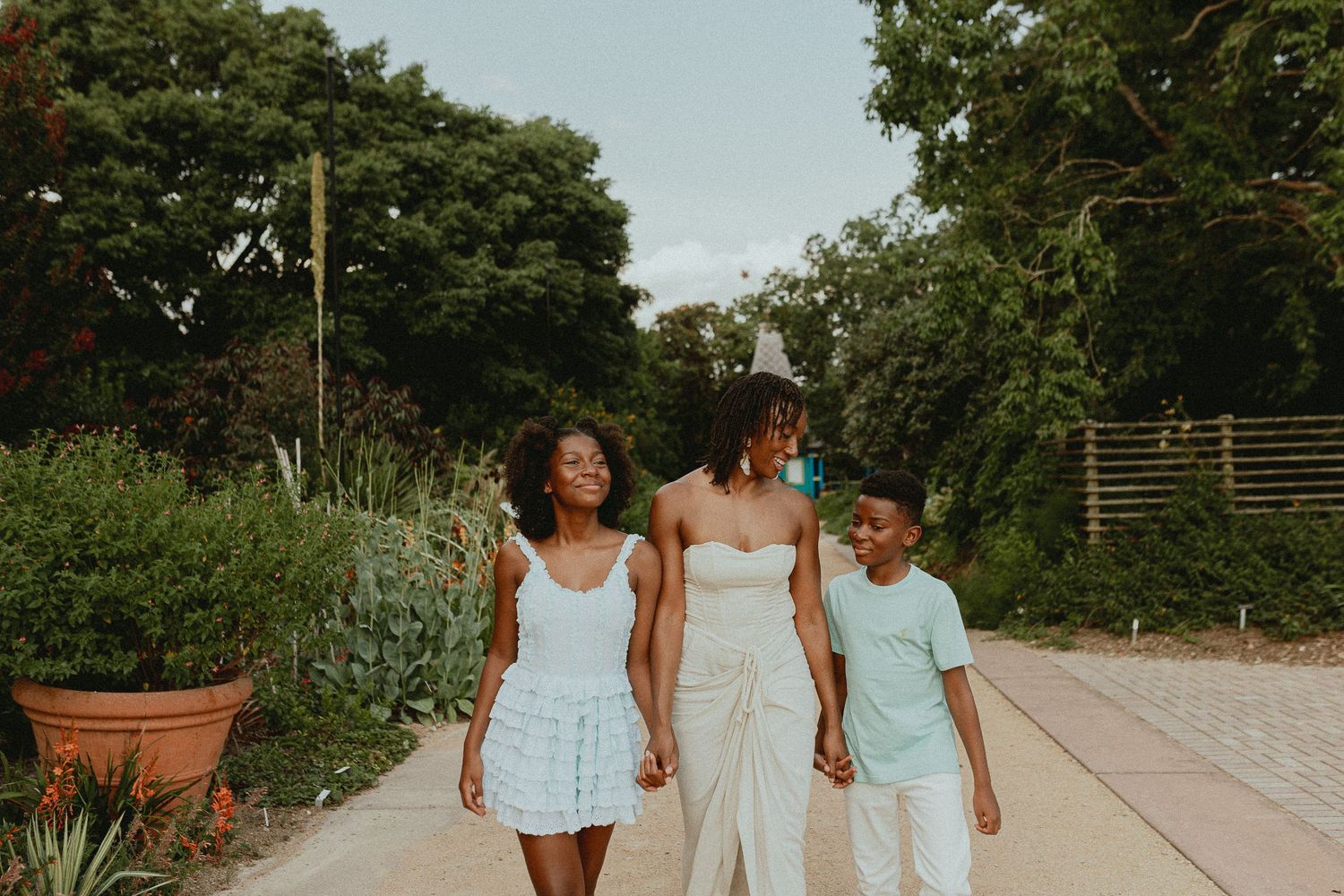 Three people walking together on a garden path surrounded by greenery.