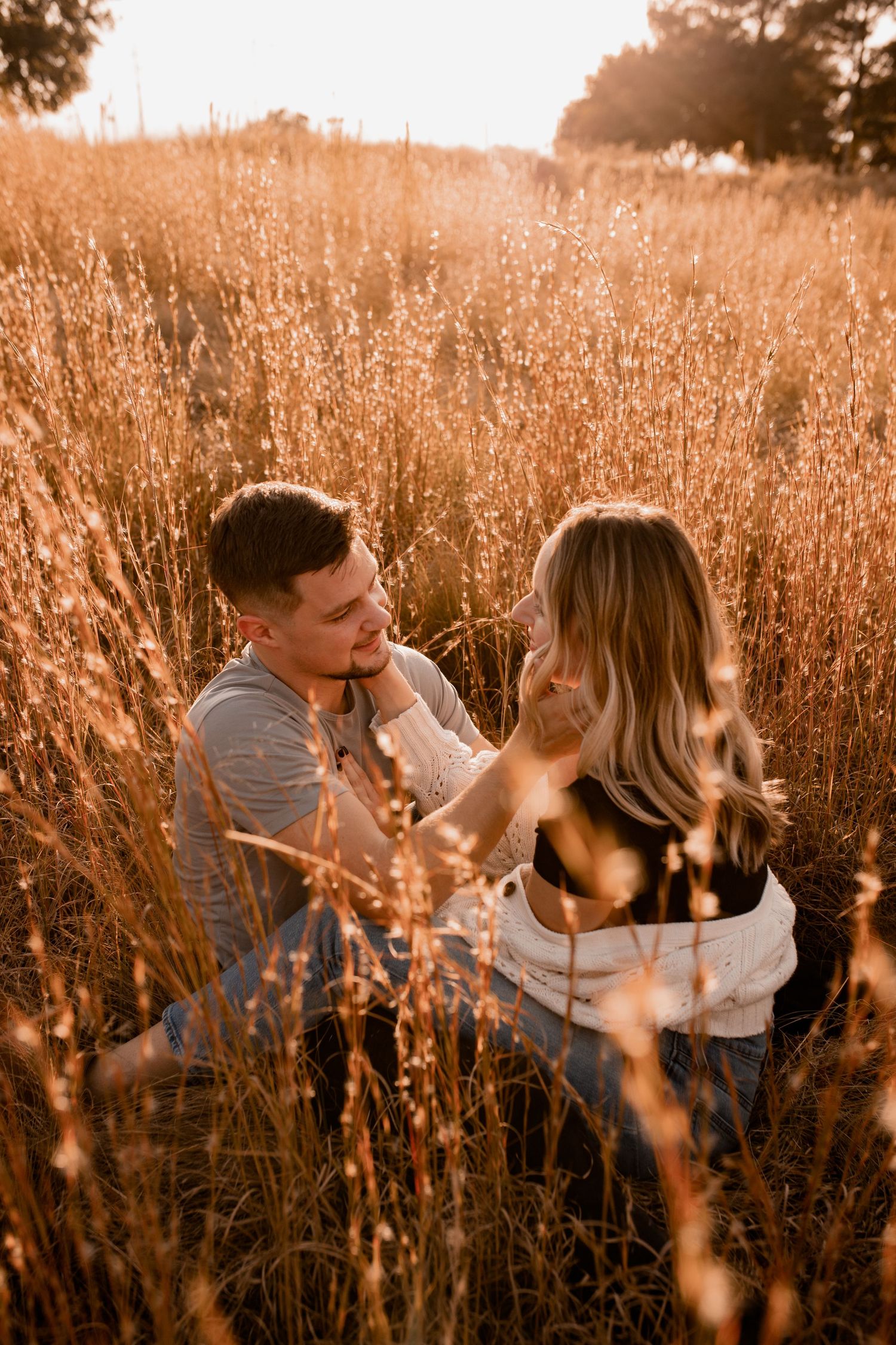 A couple embraces in a golden wheat field during sunset.