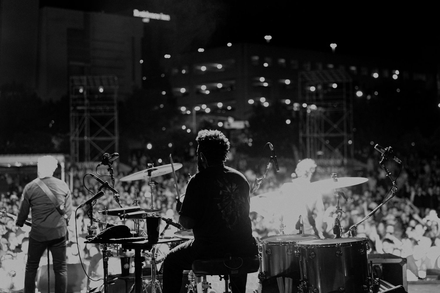 Wide concert stage shot with bright lighting and crowd silhouettes in foreground.