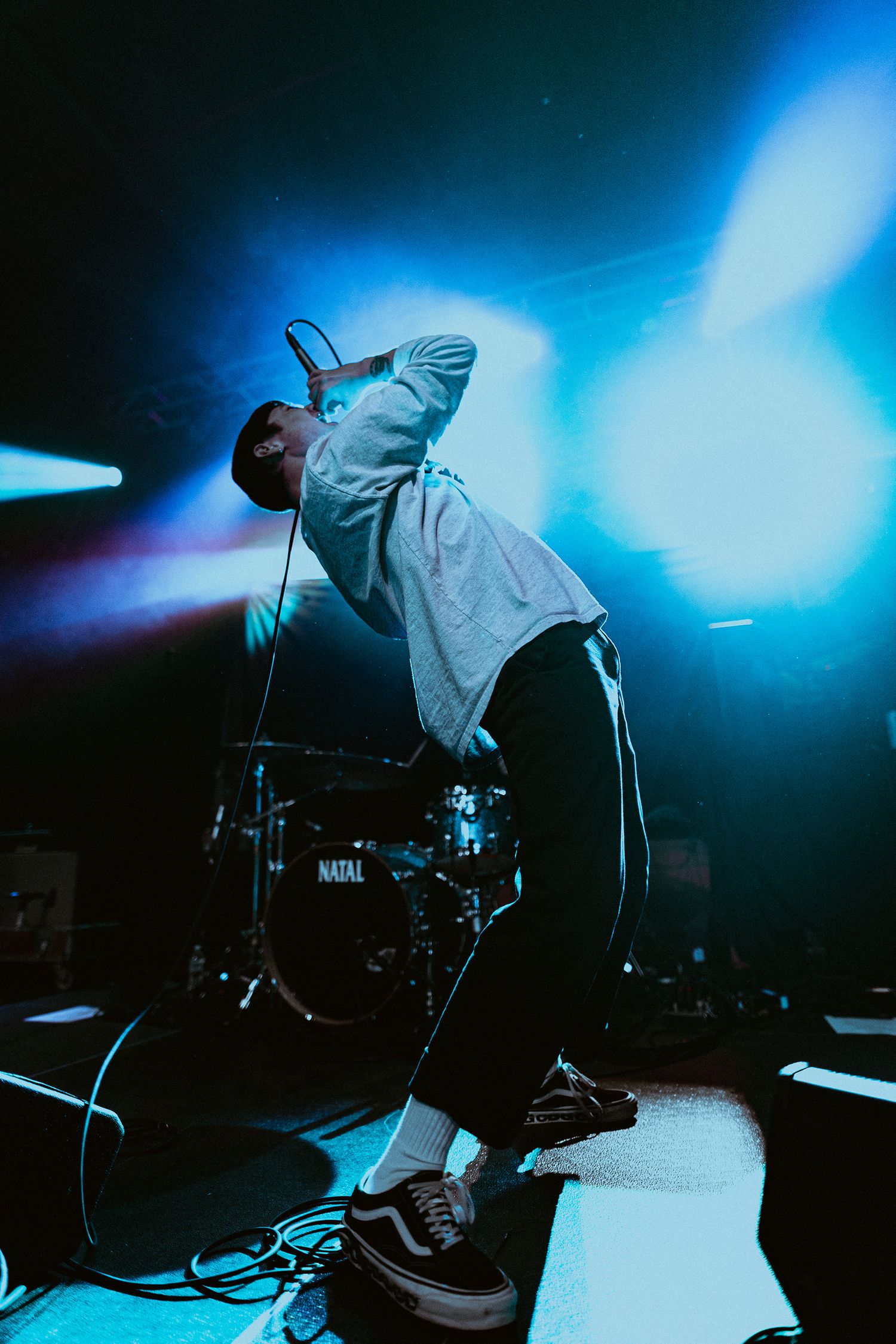 Performer in hoodie silhouetted against bright blue stage lights during dynamic show.