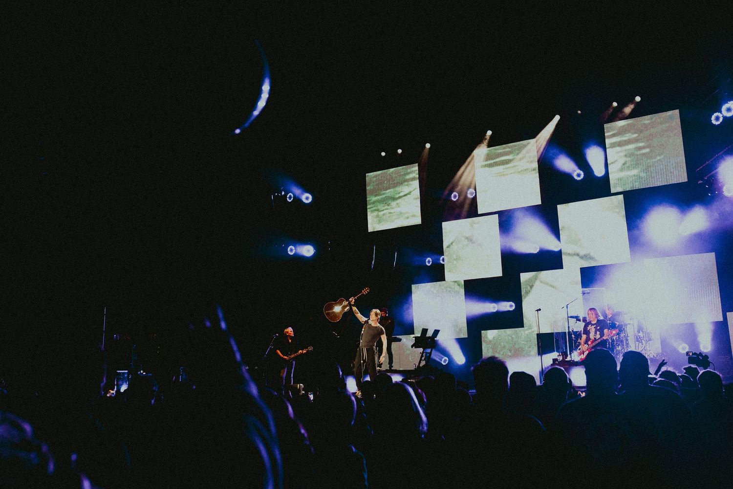 Concert venue with illuminated screens and crowd silhouettes during nighttime performance.