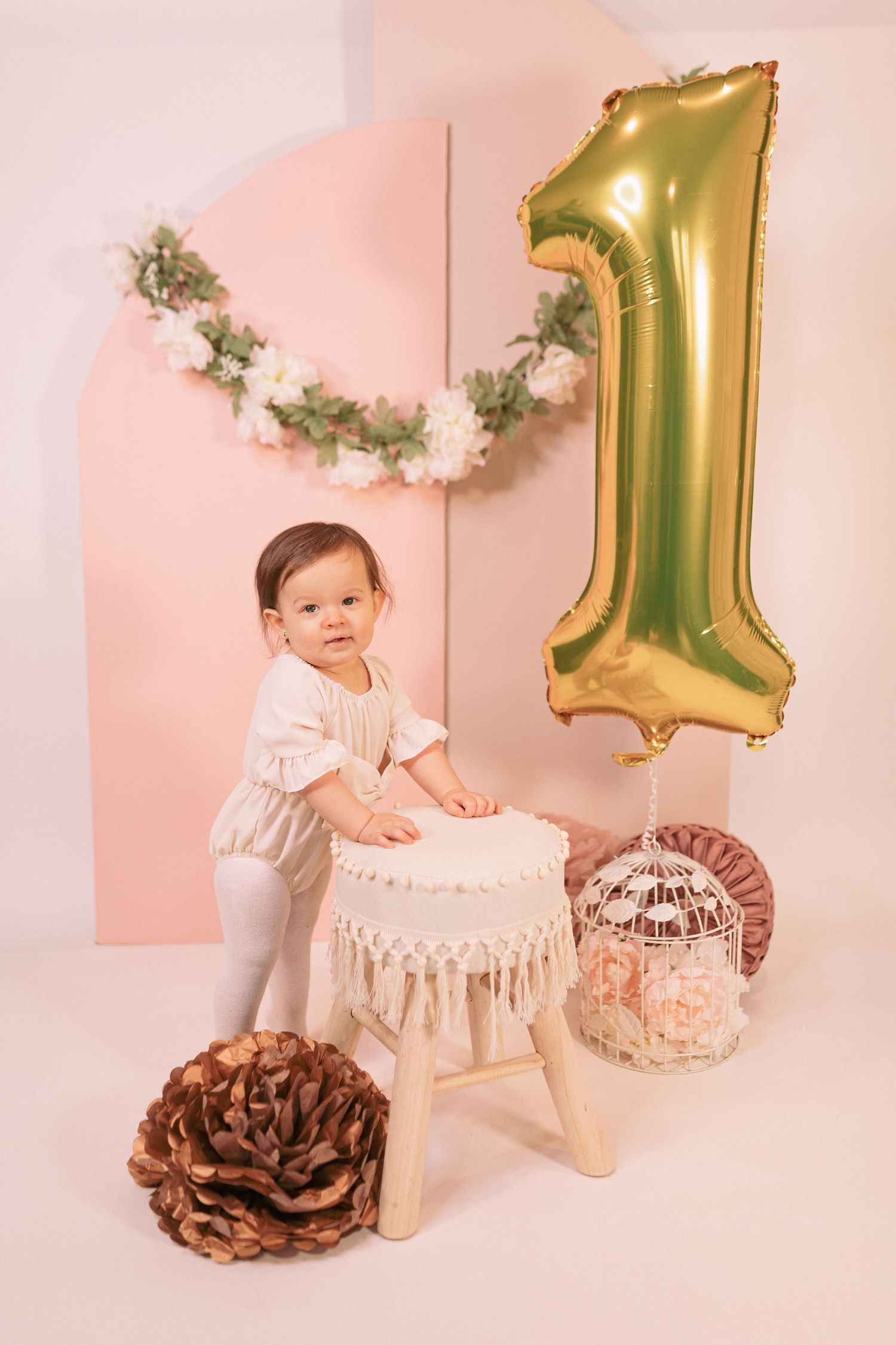 First birthday photoshoot setup with gold balloon, cream cake stand, and pink backdrop.