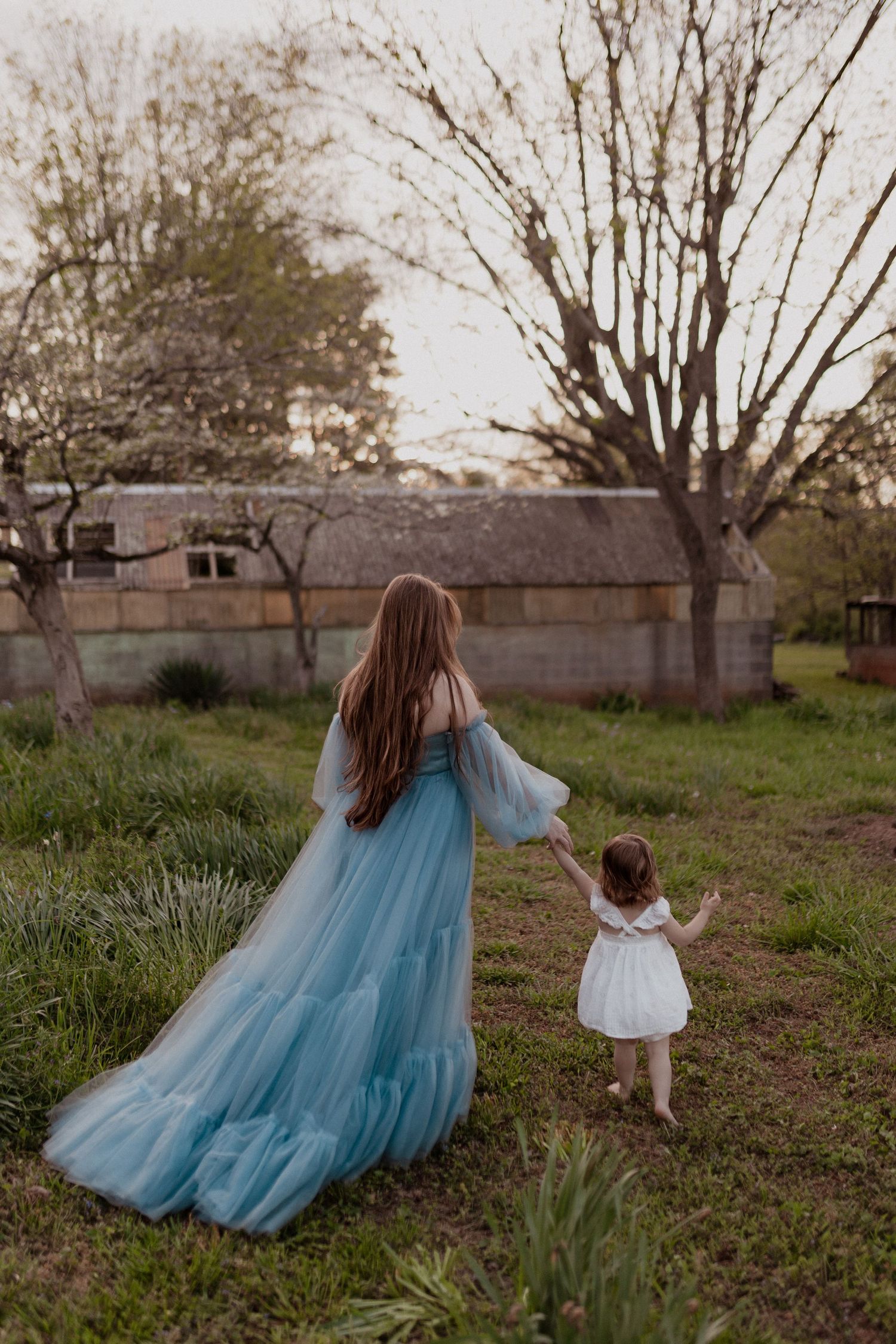 Two people in matching blue and white dresses walk through a grassy field with bare trees.