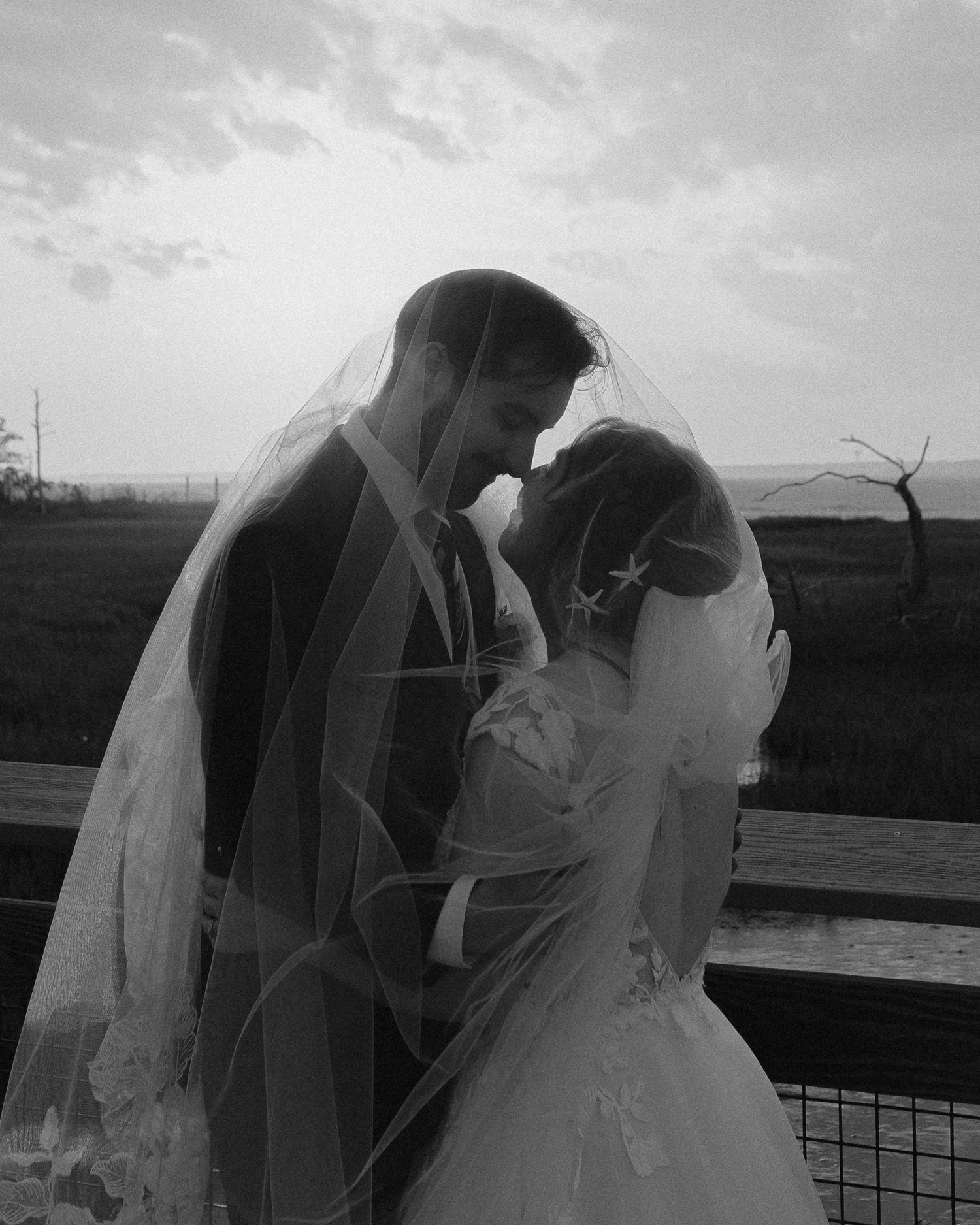 A silhouetted couple shares an intimate moment on a boardwalk at dusk.