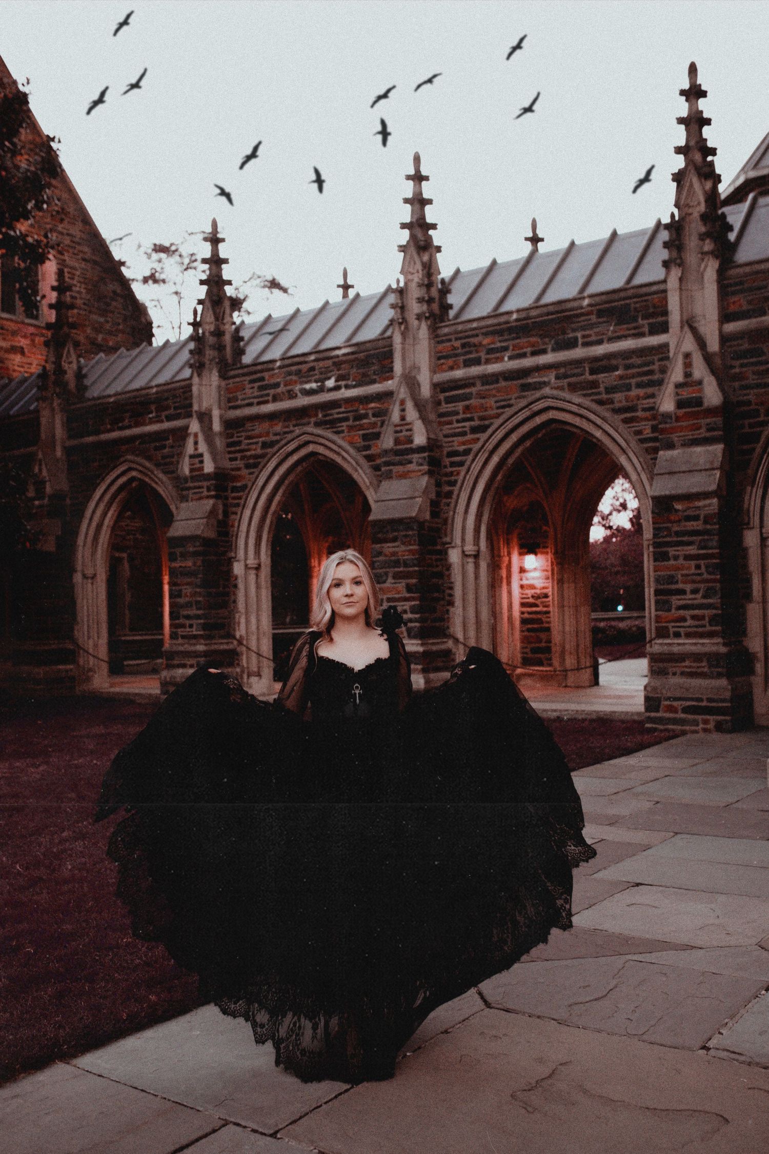 A dramatic black dress billows against gothic architecture at sunset.