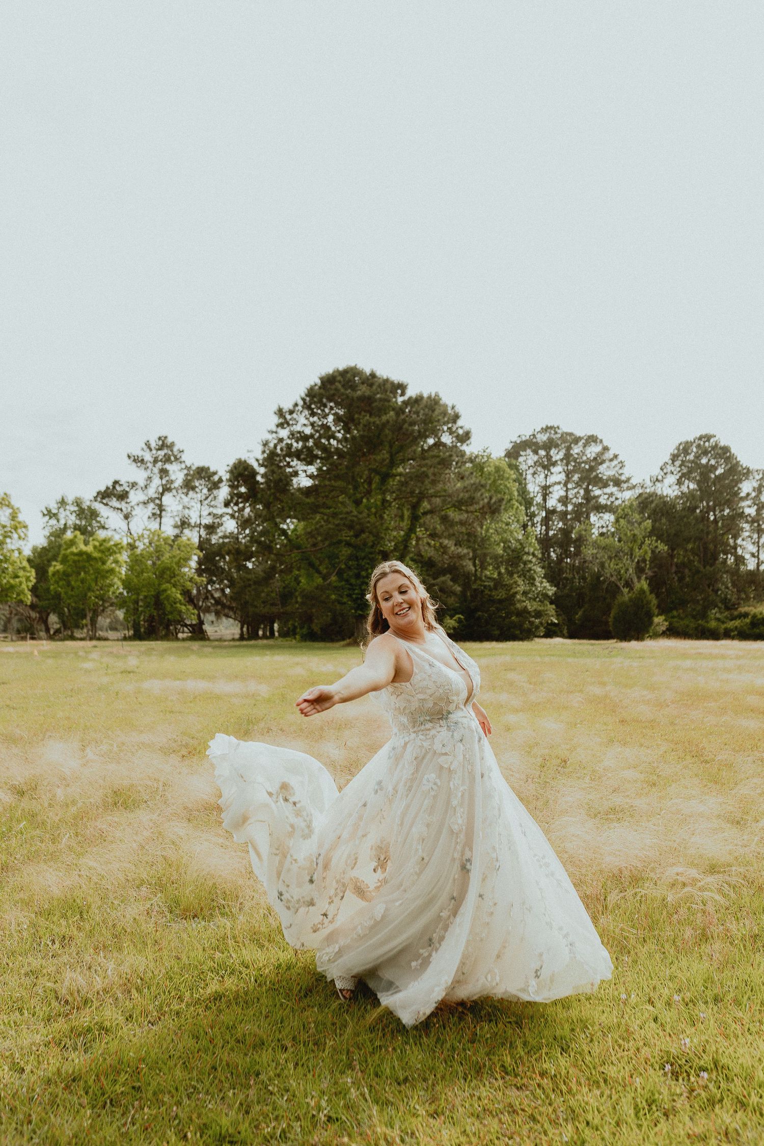 Bride twirls in lace wedding dress across sunny meadow.