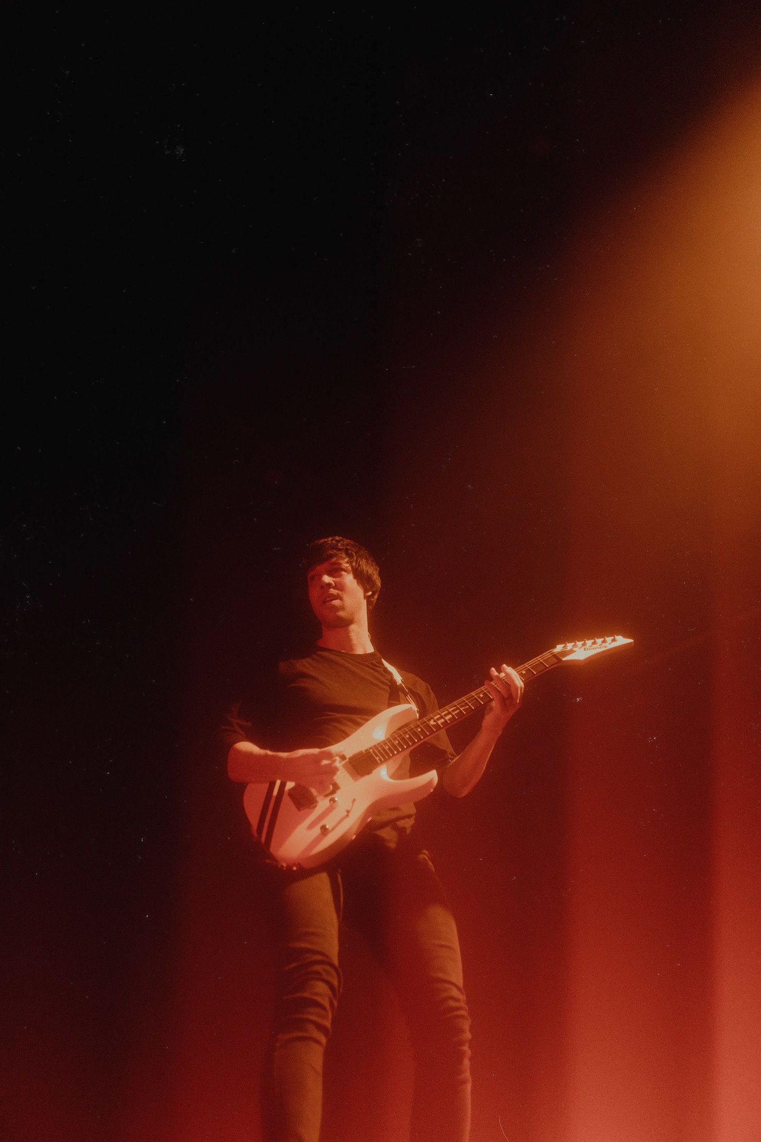 Guitar player performing on stage with dramatic orange lighting and fog effects.