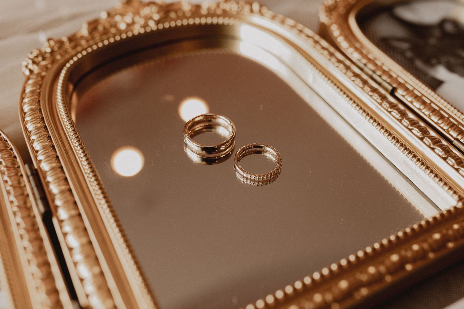 Two gold wedding bands resting on a decorative gold mirrored tray, symbolizing elegance and commitment.