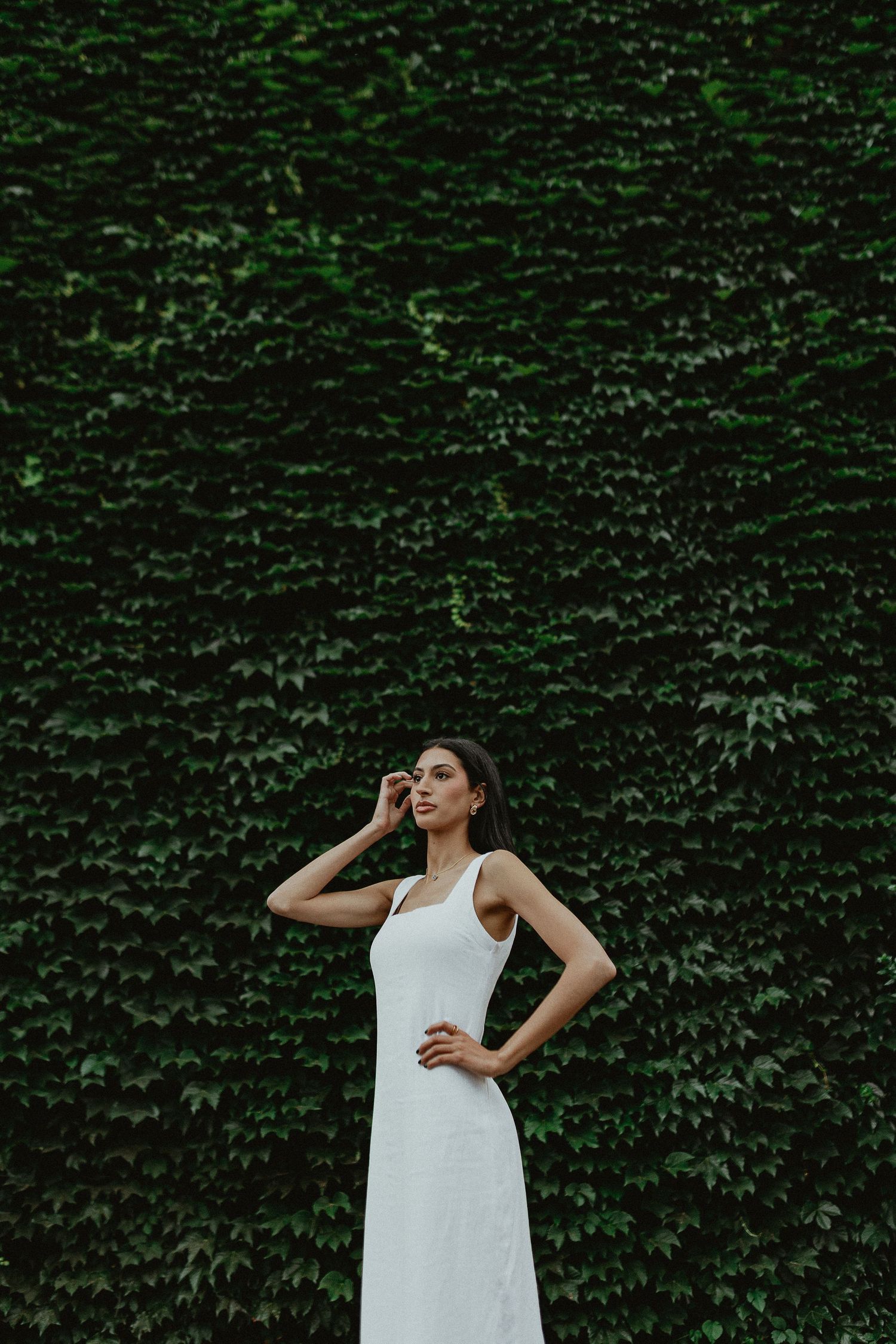 White dress contrasts against lush green ivy wall backdrop.