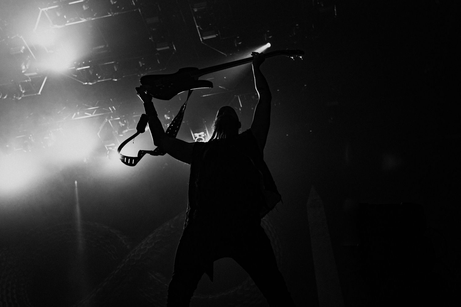 Silhouetted figure holding instrument overhead during dramatic concert lighting.